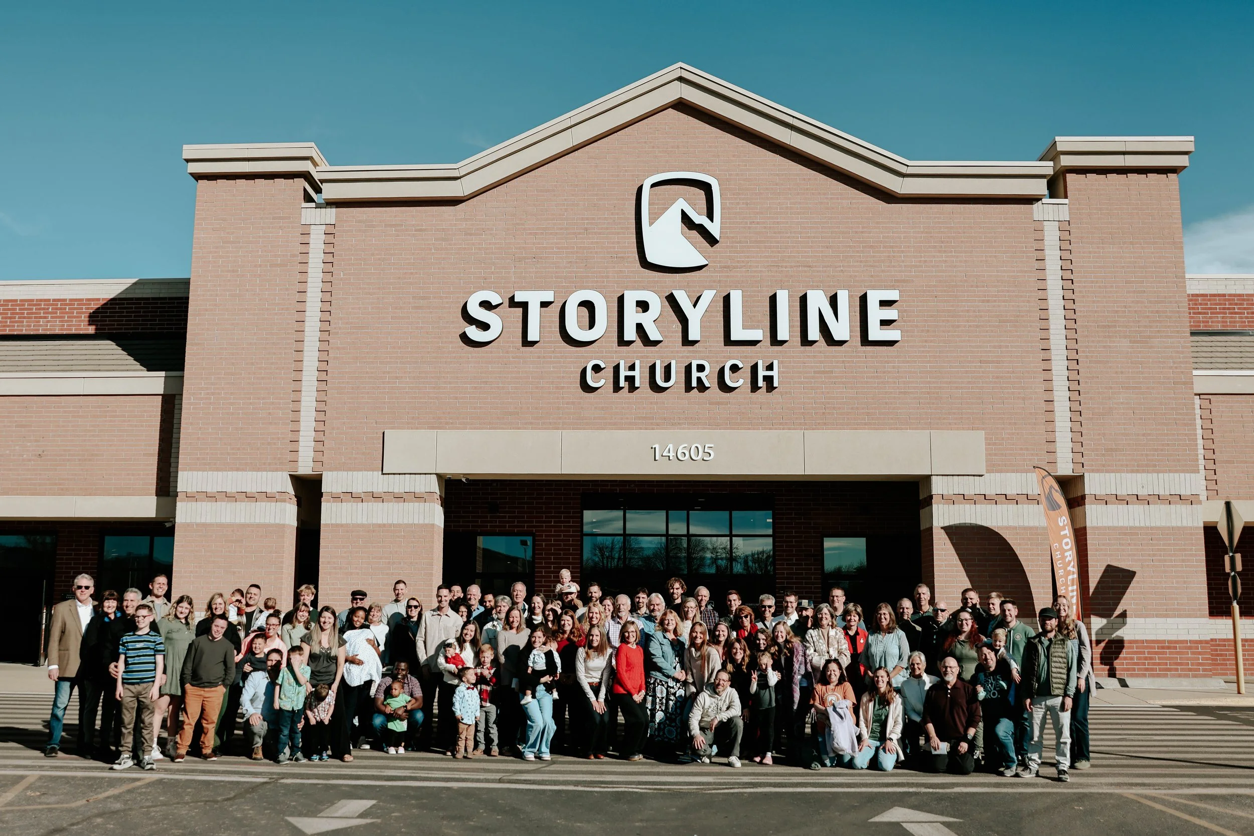 Large group of people gathered in front of the Storyline Church building with a brick facade and large sign.