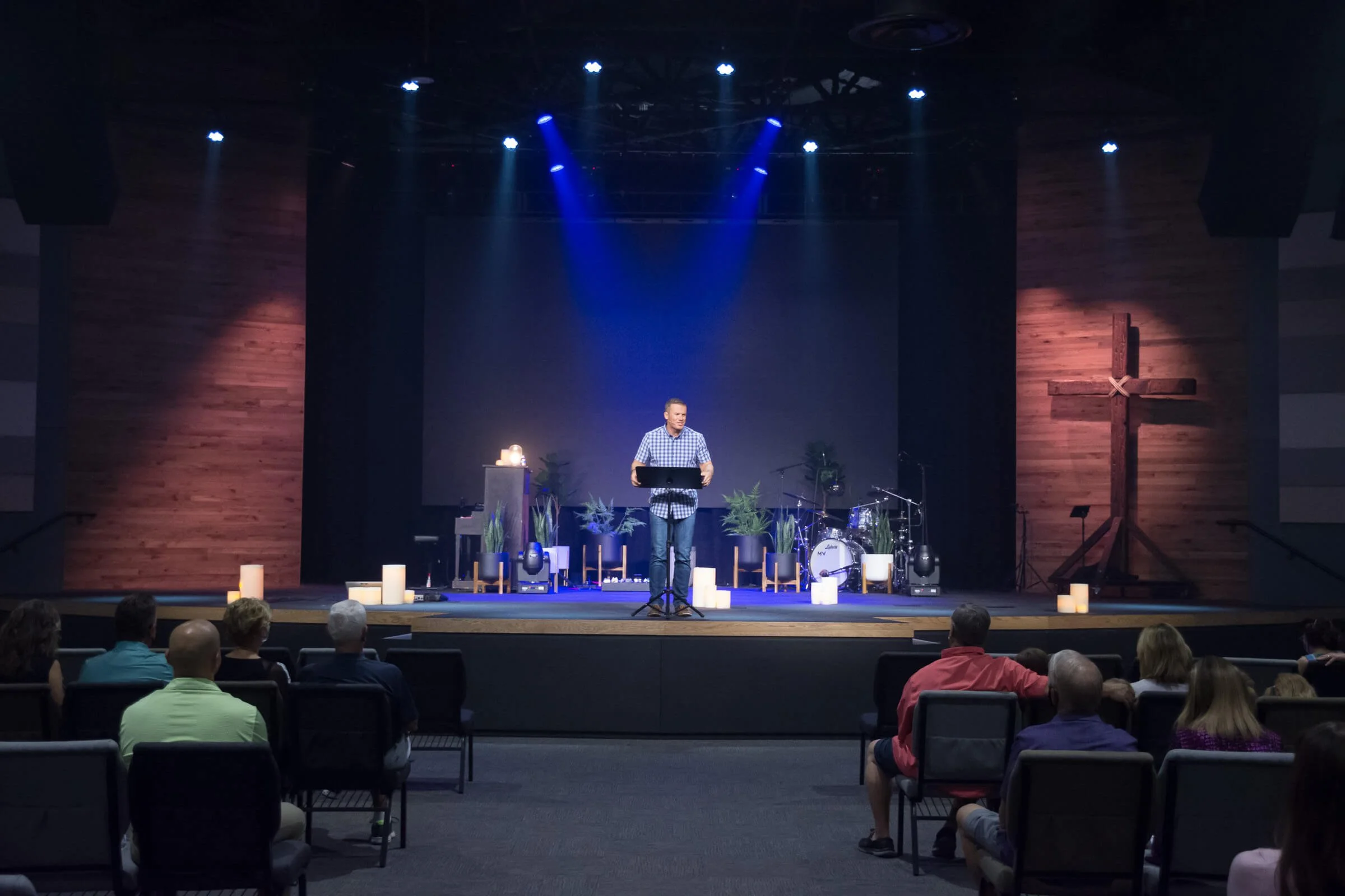 A man giving a presentation on stage with his arms outstretched, wearing a gray zip-up sweater over a collared shirt, with the text "April 2020" displayed in the upper right corner.