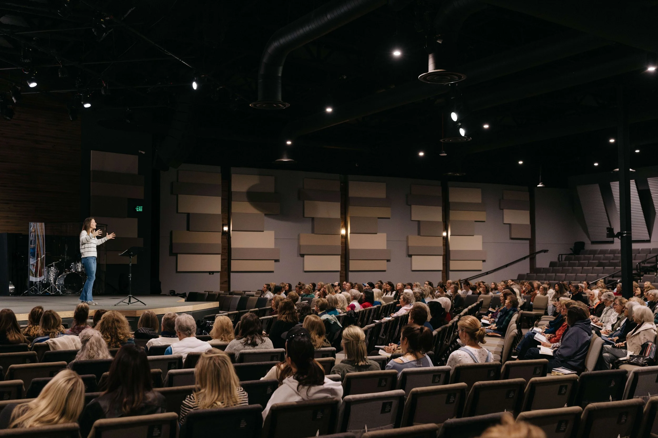 A speaker on stage addressing an audience in a large auditorium.