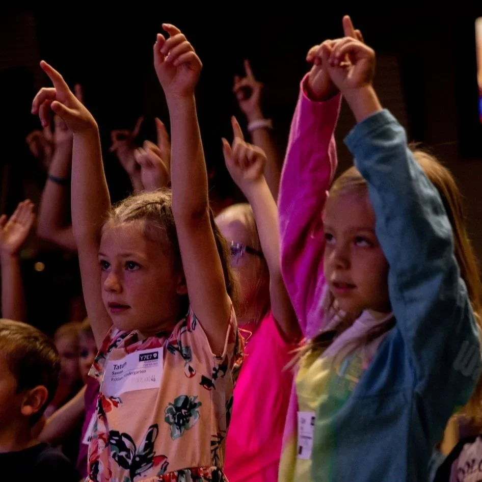 Group of children raising their hands in a classroom or event.