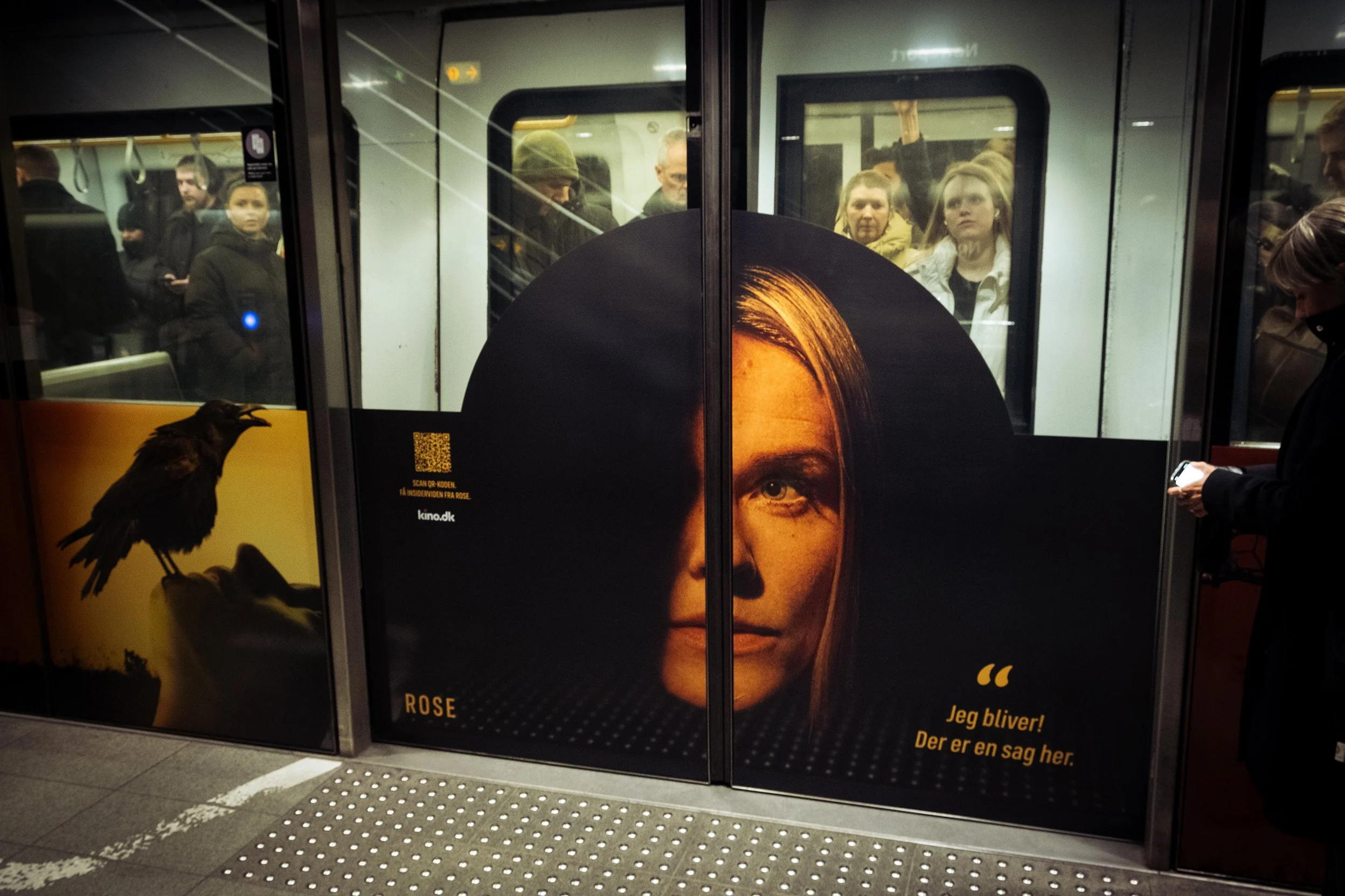 Reklameplakat i metro med ansigt af en kvinde og teksten 'Jeg bliver! Der er en sag her.'
