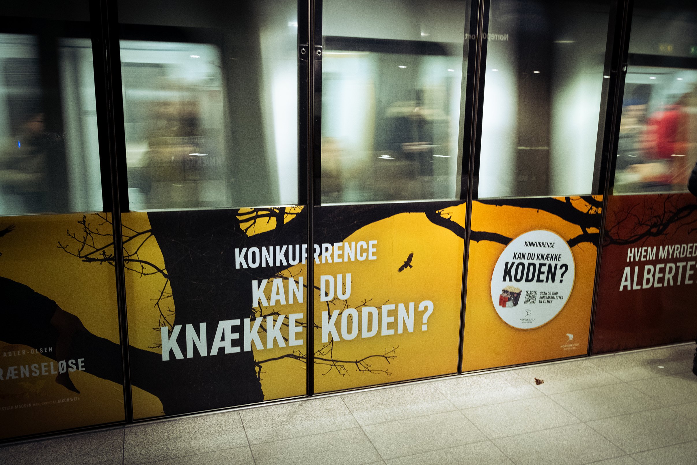 Annonce på en glasdør med teksten 'Konkurrence kan du knække koden?' med en baggrund af en trægren og en fugl, der flyver.