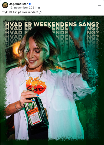 Ung kvinde med blond, skulderlangt hår, smilende, iført hvid skjorte, holder en flaske Jägermeister og løfter sin arm op. Baggrund med tekst 'HVAD ER WEEKENDENS SANG?'