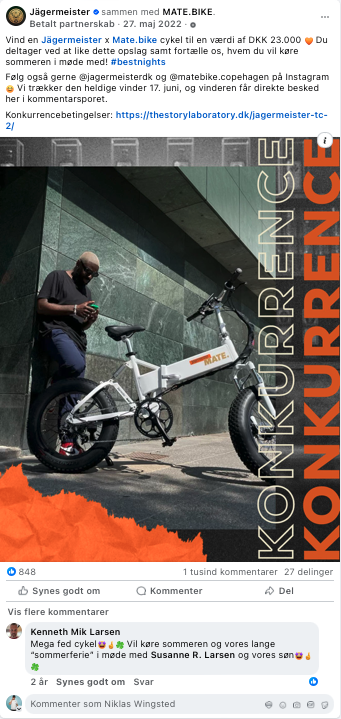 En mand står ved en JÆGERMEISTER MATE BIKE cykel udenfor en bygning, der har en stor skiltning, der siger 'KONKURRENCENCENTER'.