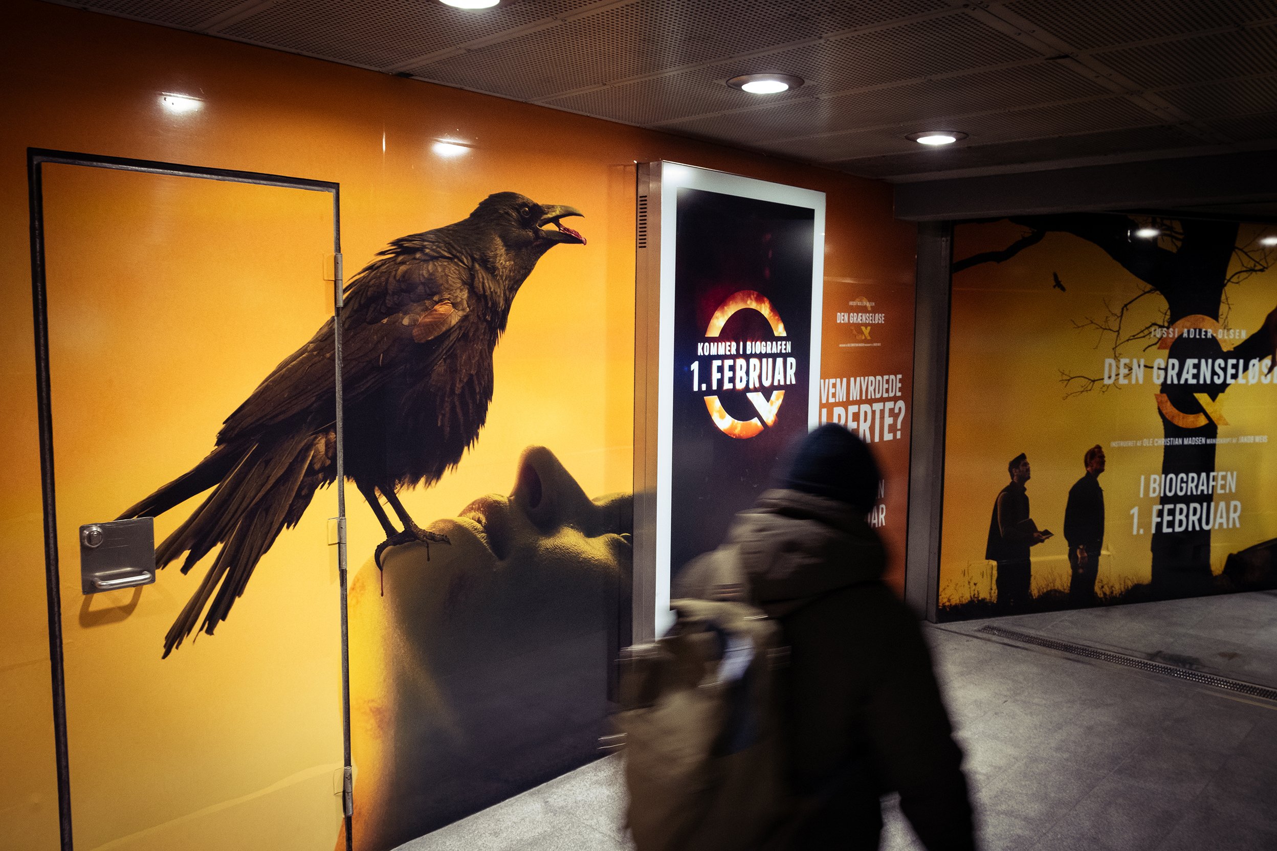 Tegnet væg med en stor ørn, der står på en persons ansigt, mens en person går forbi i forgrunden.