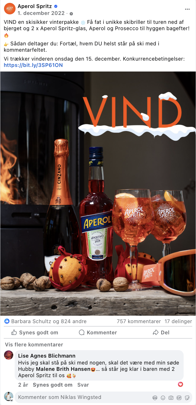 Billedet viser en flaske Aperol, en flaske Prosecco, to Aperol Spritz-drinks i glas med is og citron, nødder, et par ski-briller og en juledekoration med små pommer. Der er også skrevet 'VIND' med overskæg af sne over teksten.