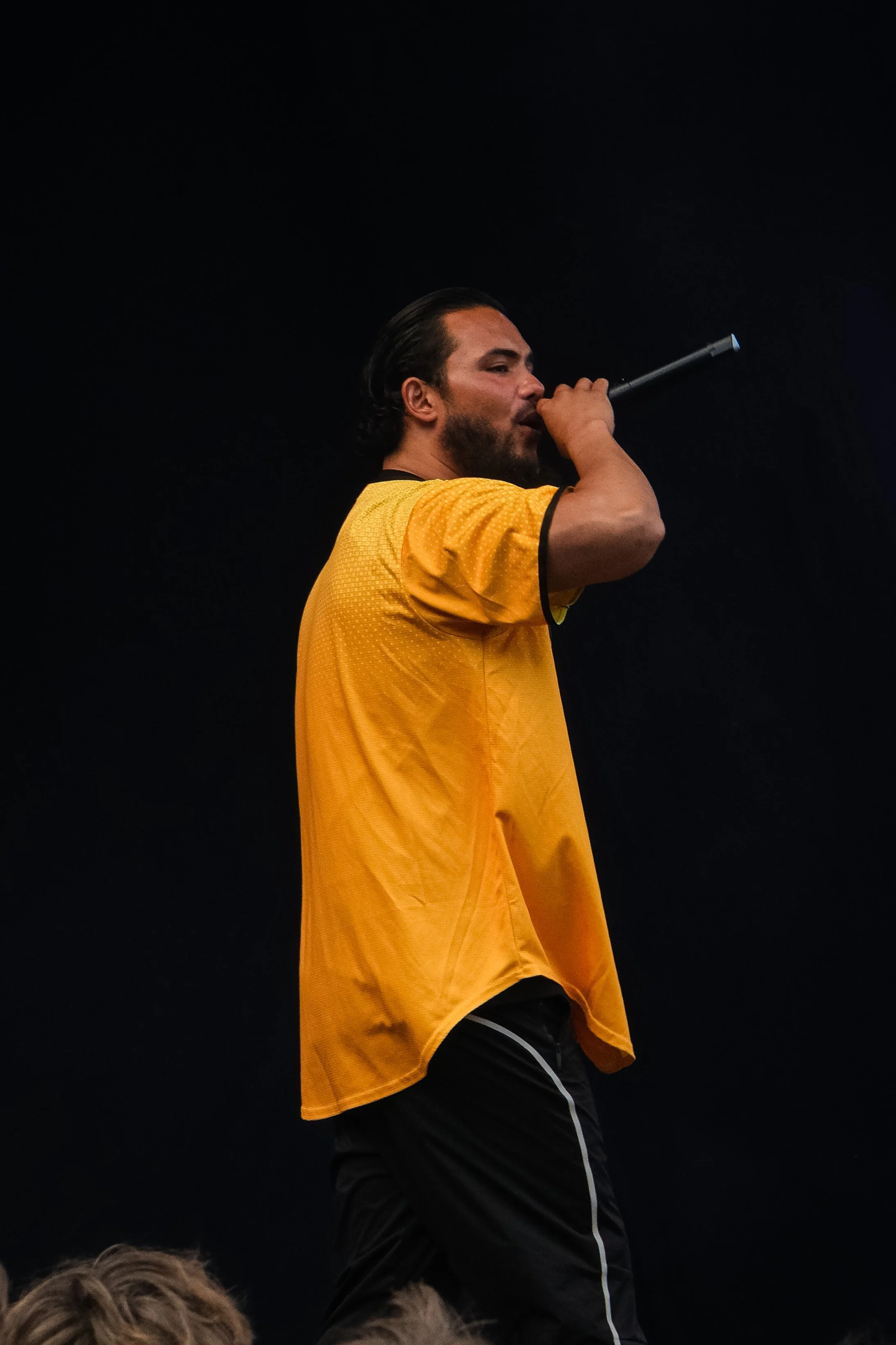 Mand i en gul sporttrøje der synger med og bruger en mikrofon.