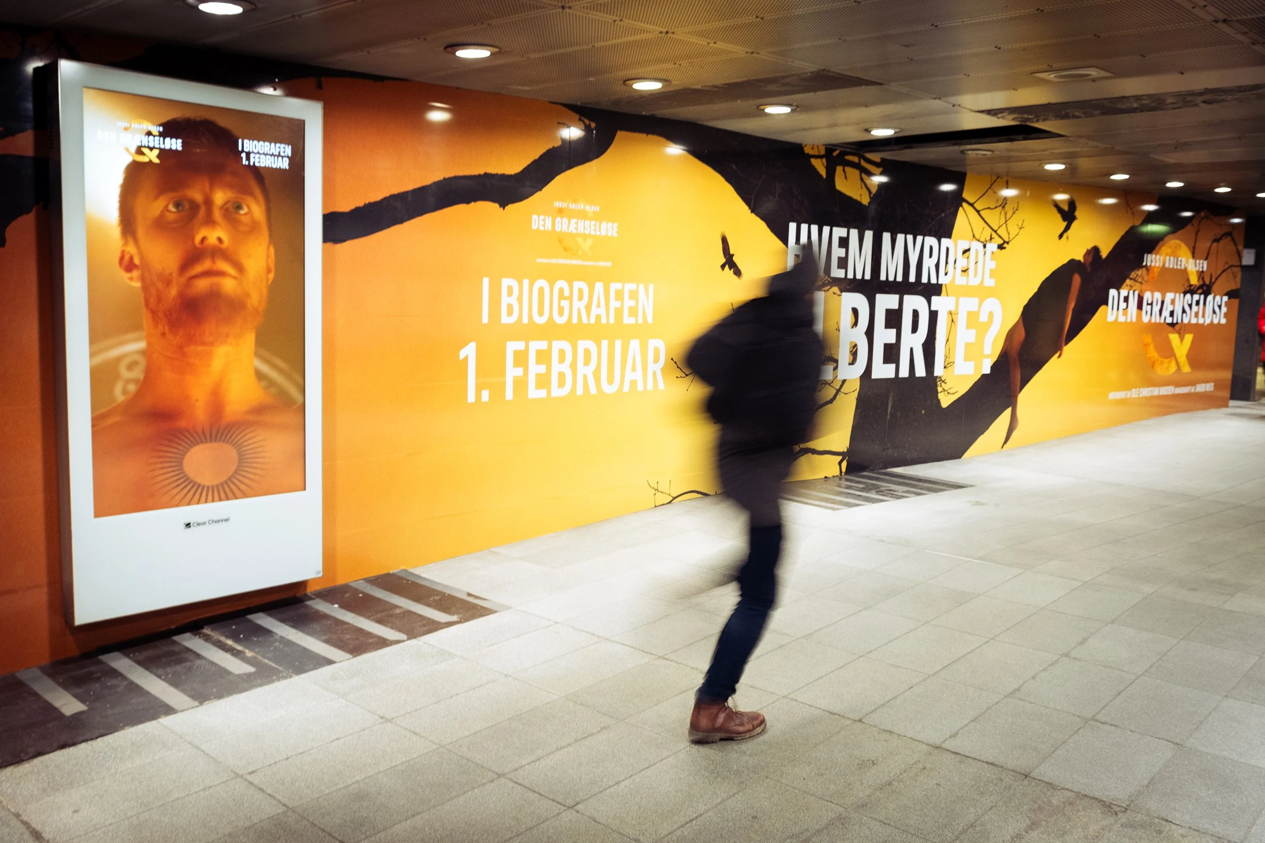 Person i bevægelse foran en reklamevæg med plakater og tekst om biografpremiere den 1. februar.