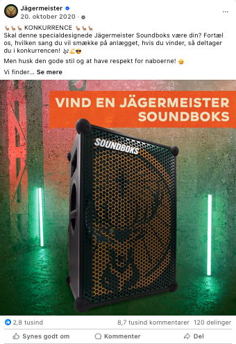 Billedet viser en Jägermeister Soundbox, en bærbar højtaler med et grafisk design, der promoveres med teksten 'VIND EN JÄGERMEISTER SOUNDOK'. Baggrunden har grønne og røde lys og en grå væg.