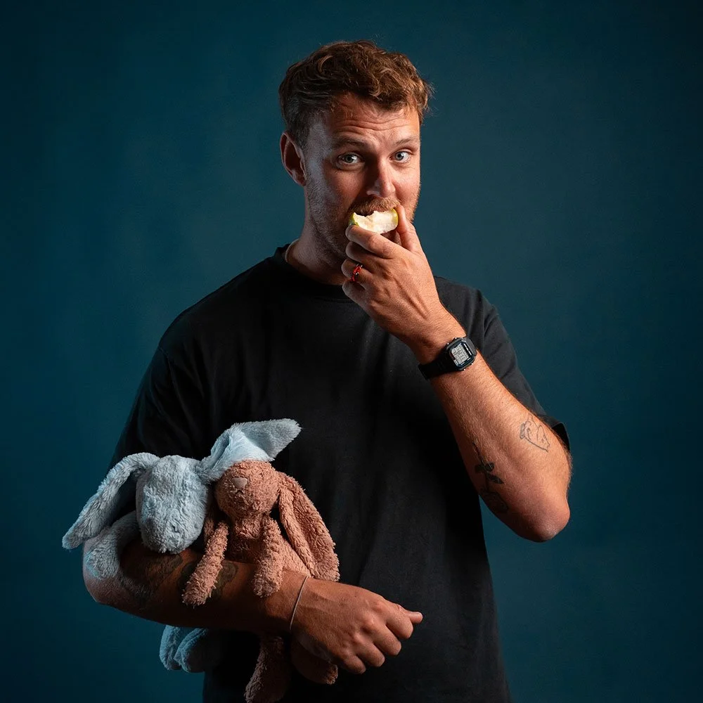 Mig (Niklas Wingsted) , i sort T-shirt, holder to bamser og spiser et æble. Bag ham er en mørk blå baggrund.