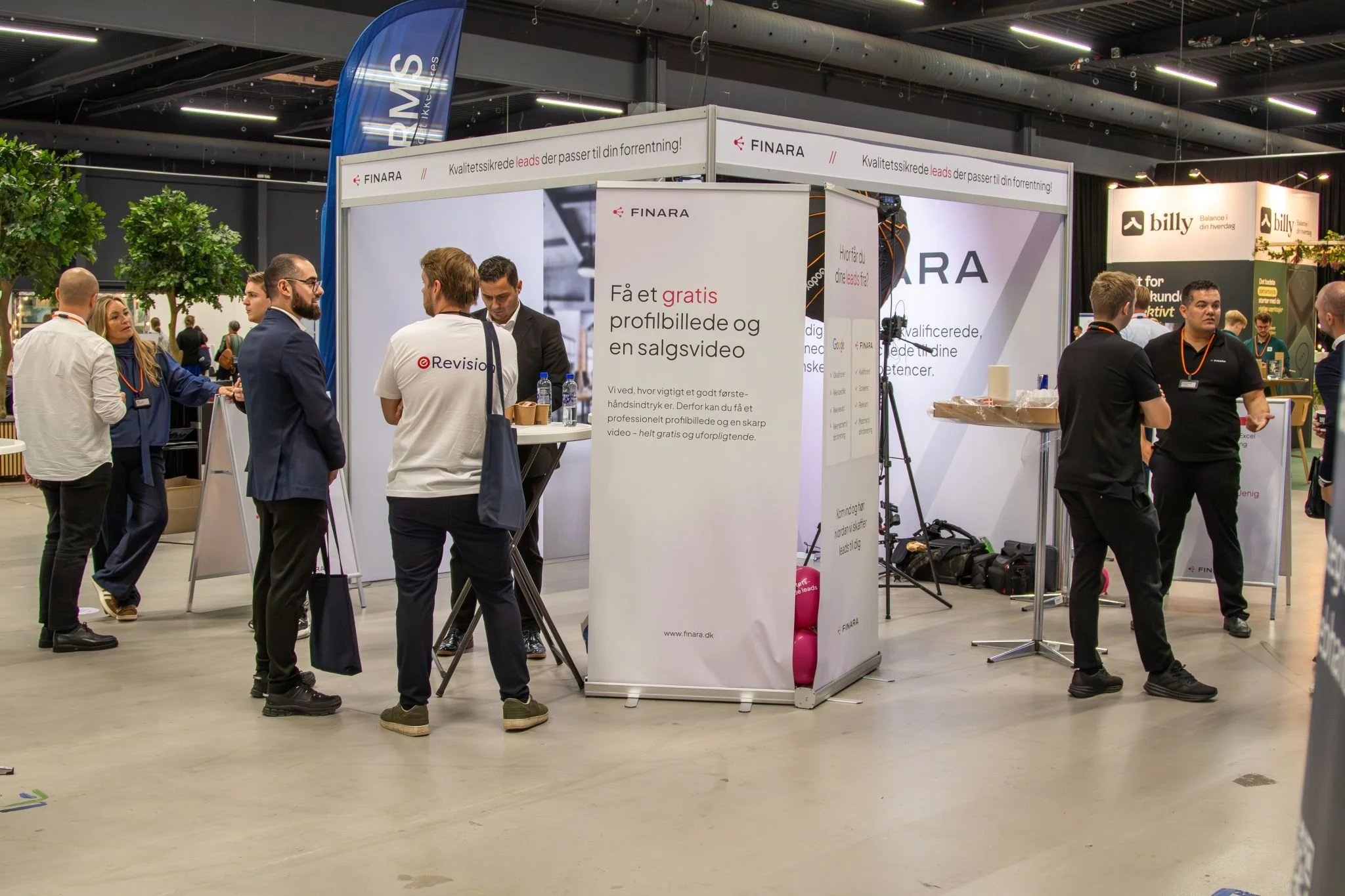 Mennesker taler ved en messestand med logoet 'FINARA' og info om gratis profil- og salgsvideo på en messe.