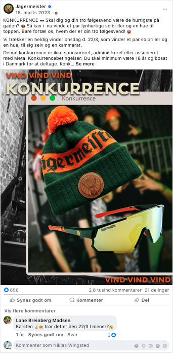 Person iført en grøn og orange Beanie med Jägermeste logo, som holder en umbrella med teksten 'Jägermeste' og et par beskyttelsesbriller, del af en konkurrence.