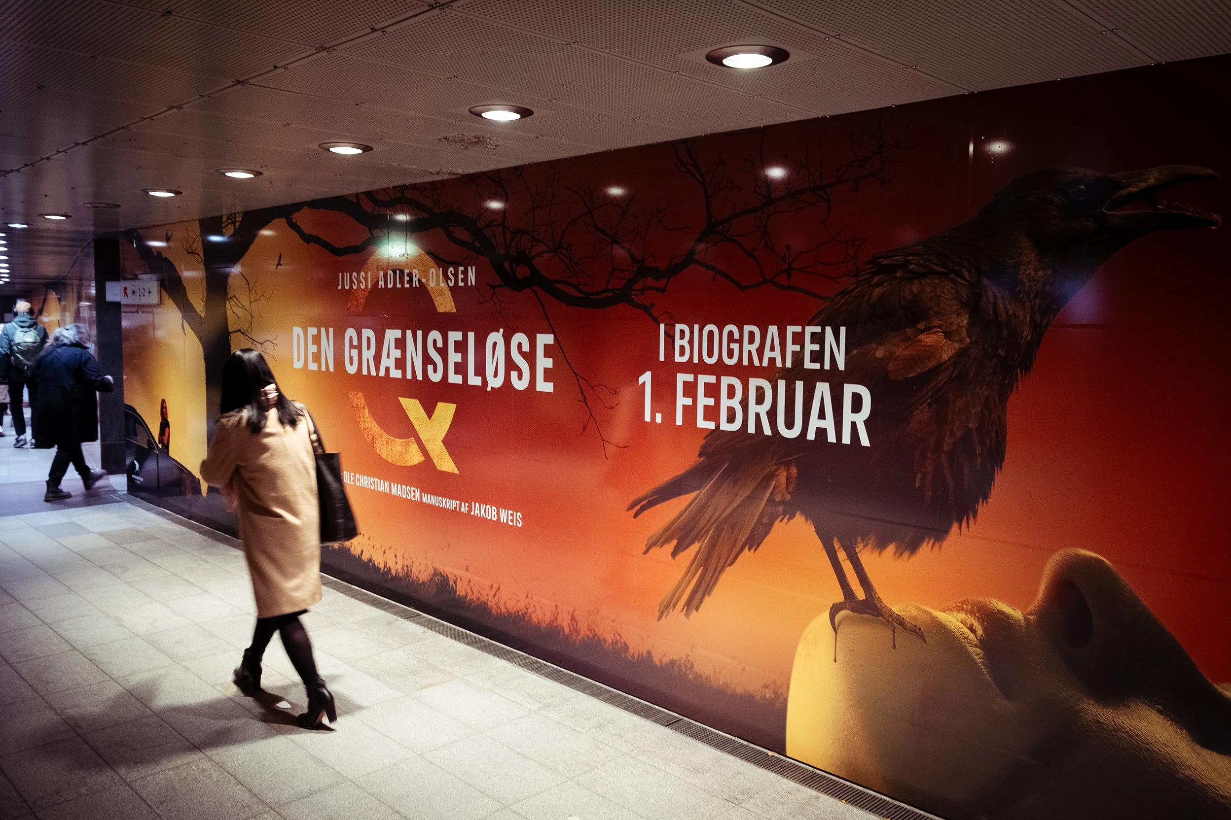 Billboard i en undergrundsstation med tekst om en filmudstilling, der viser en ravn, en sort trægren og en gylden baggrund.