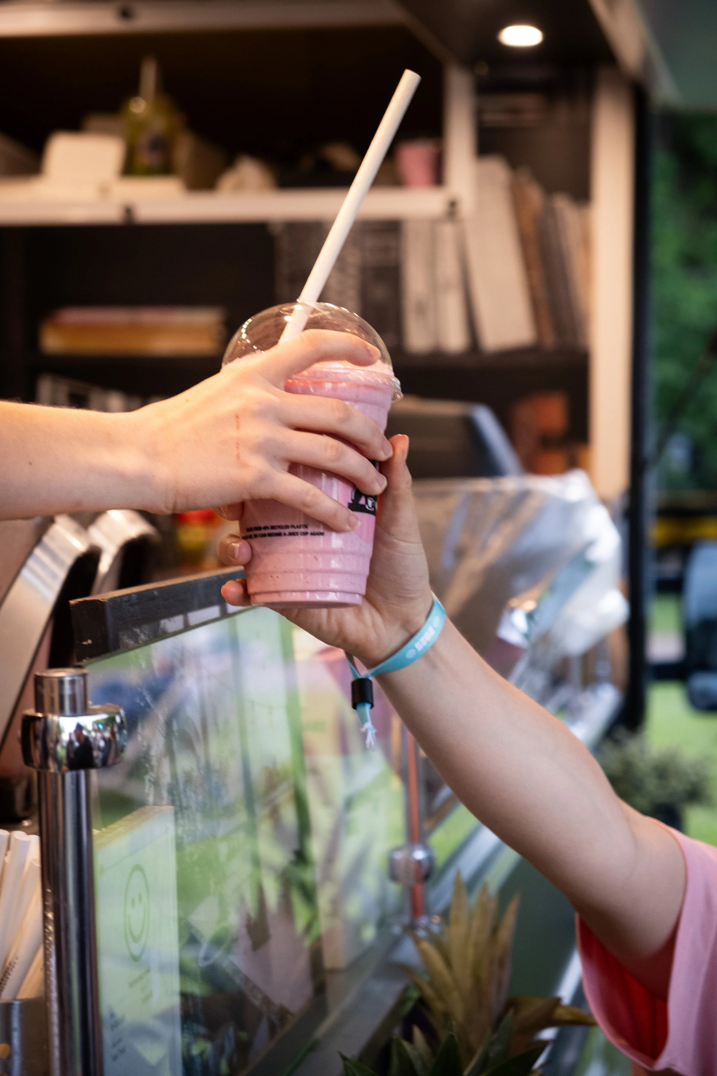 En person sender en pink milkshake til en anden person ved en isbod.