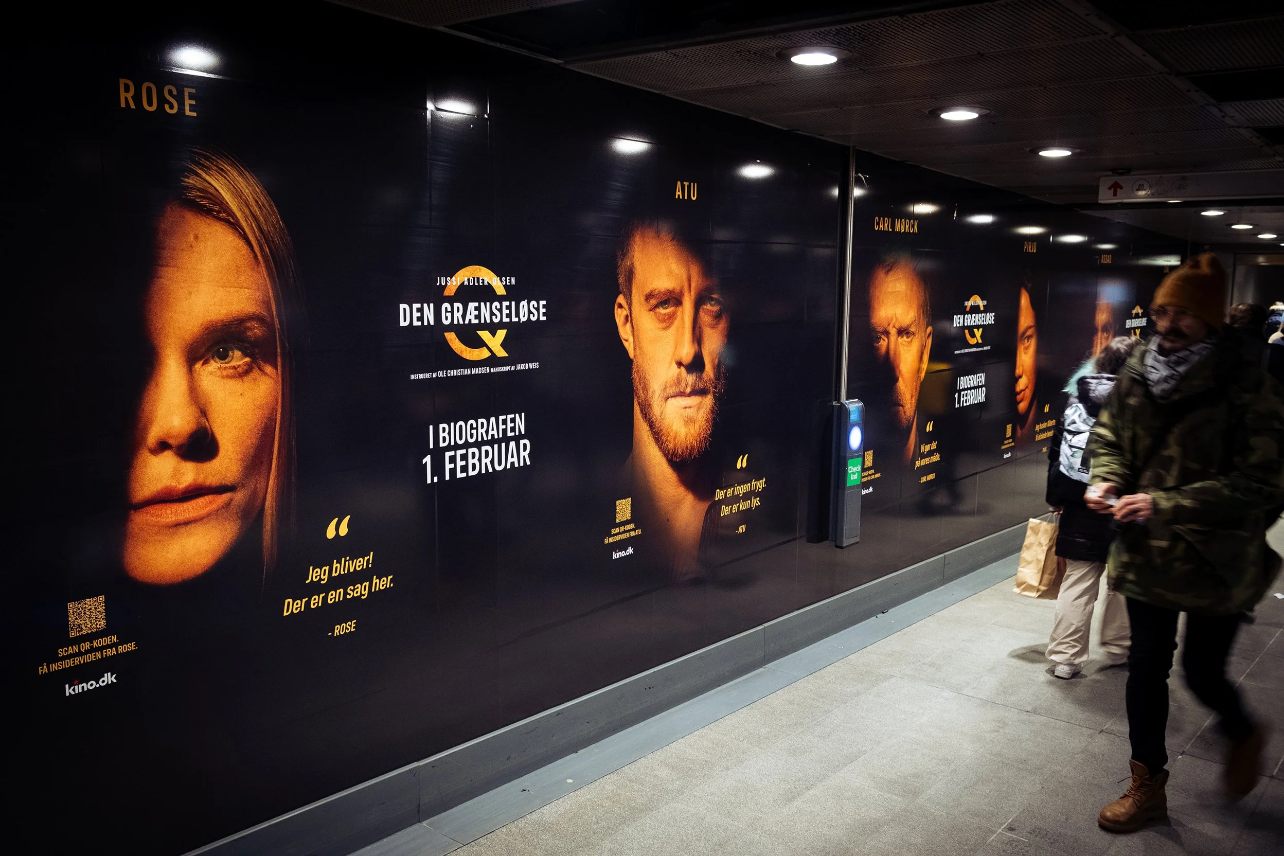 Reklameplakat for filmen 'Den Grænseløse' i en metrostation med billeder af tre skuespillere og oplysninger om premieredatoen den 1. februar