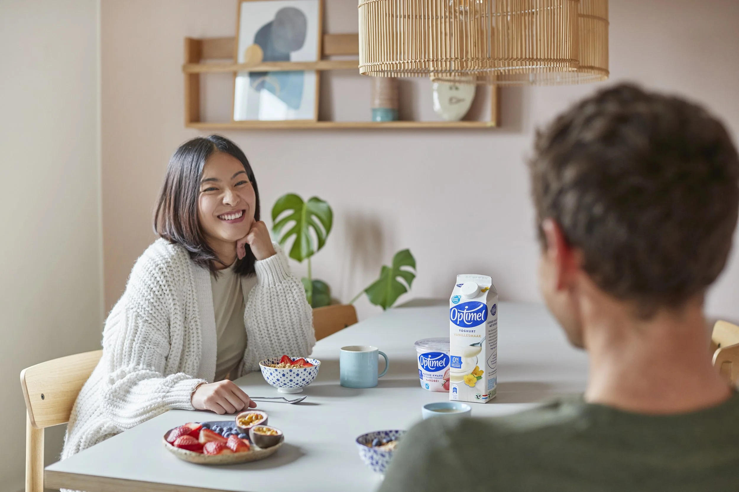 To personer sidder ved et spisebord med morgenmad og yoghurt. Den ene person ser glad ud.