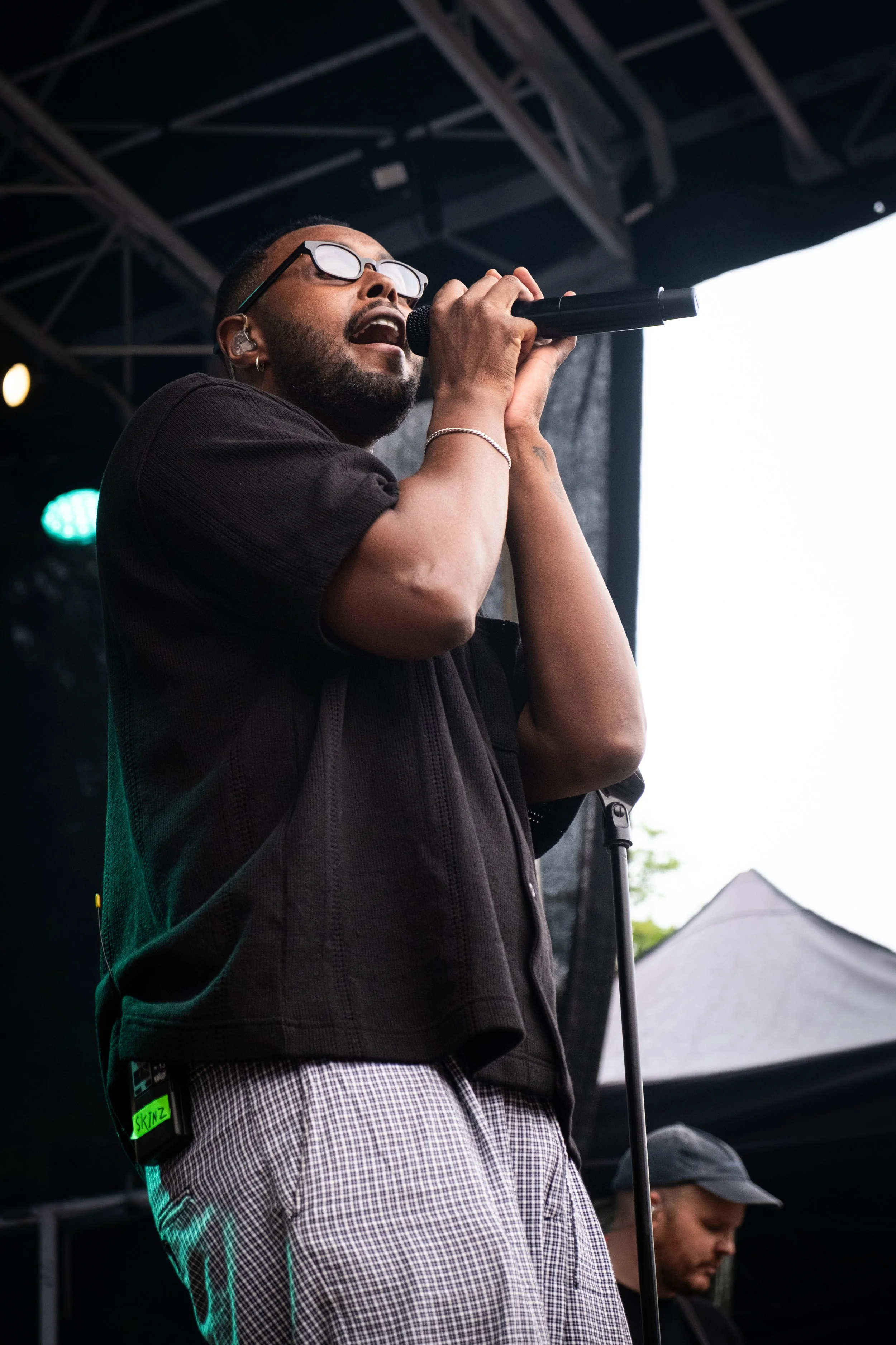 En mand synger i mikrofon på en scene under en koncert, iført briller og et sort outfit.