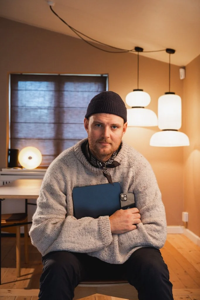 Mand sidder i et rum med moderne lyskilder, holder en smartphone og en tablet.