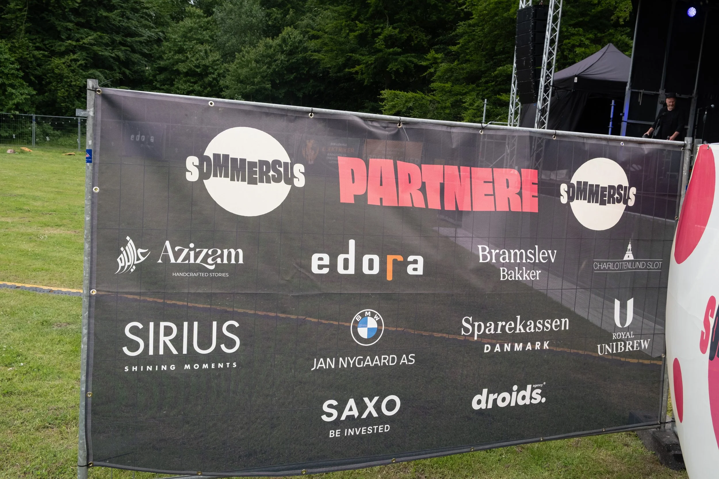 Banner med flere sponsorlogoer og teksten 'PARTNERE' ved en udendørs koncertscene.