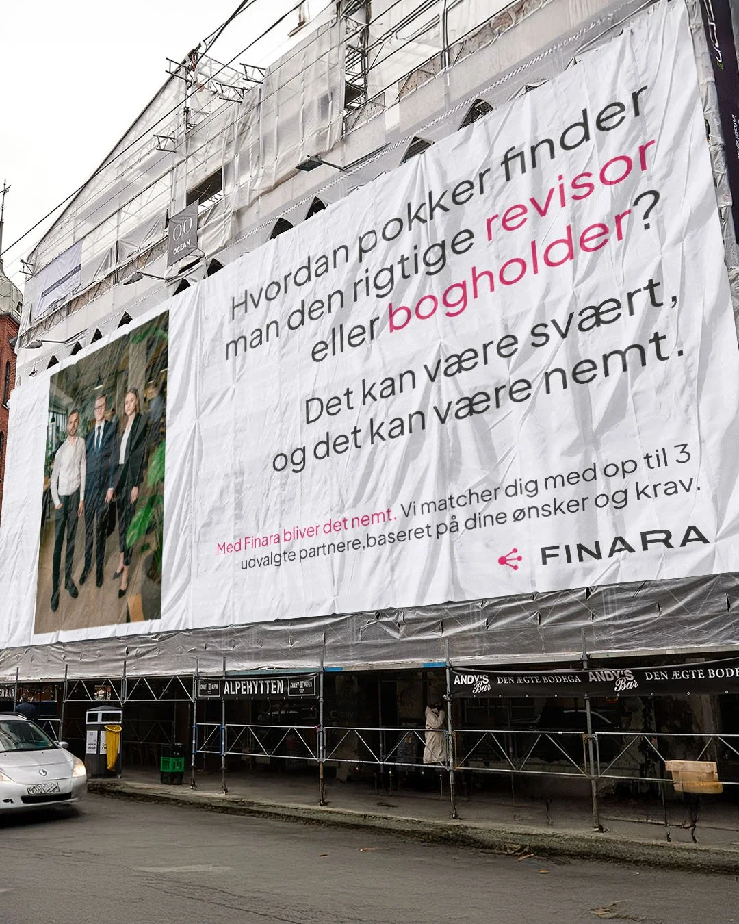 En stor reklameskærm på en bygning med en gruppe mænd iført forretningsklæder, og teksten 'Hvordan pokker finder man den rigtige revisor eller bogholder? Det kan være svært, og det kan være nemt.'