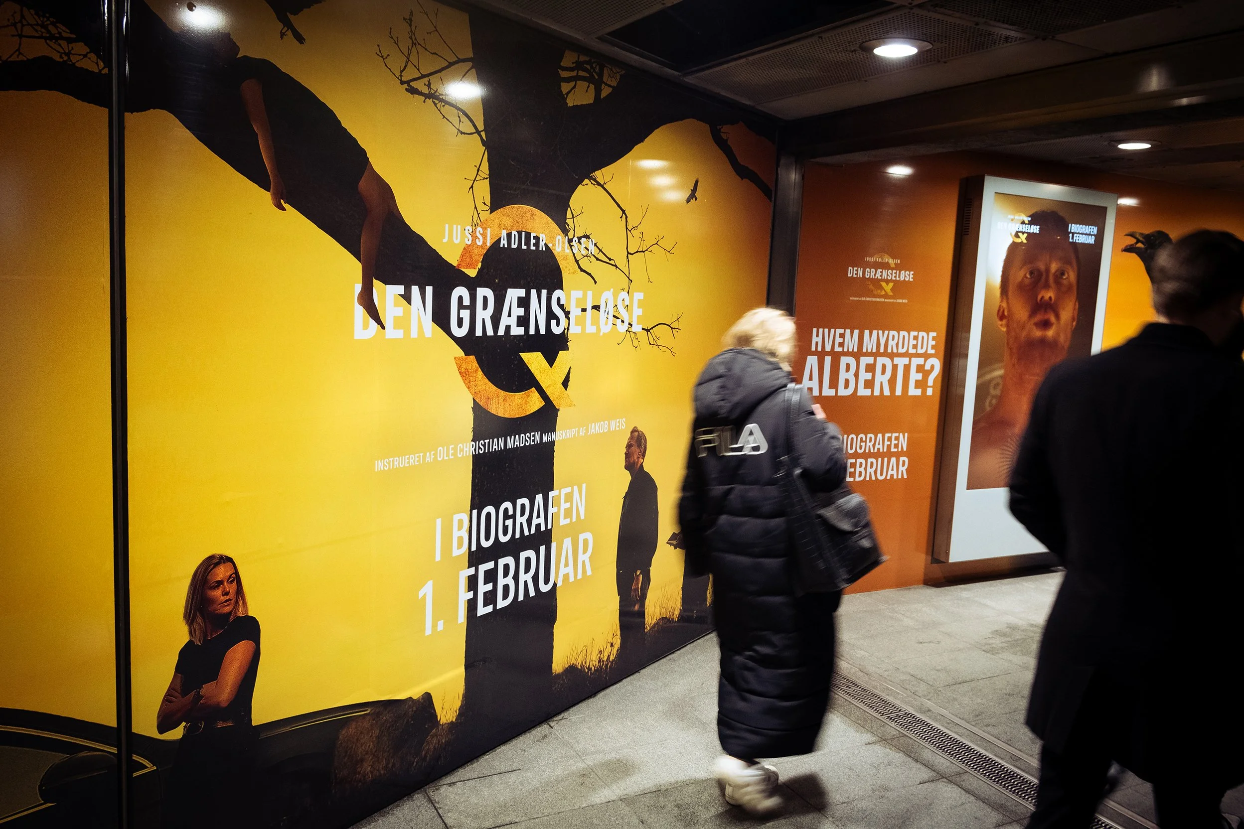 Reklametavler for biograffilm 'Den Grænseløse' med datoen 1. februar og billeder af to personer, en kvinde og en mand, på en metrostation.