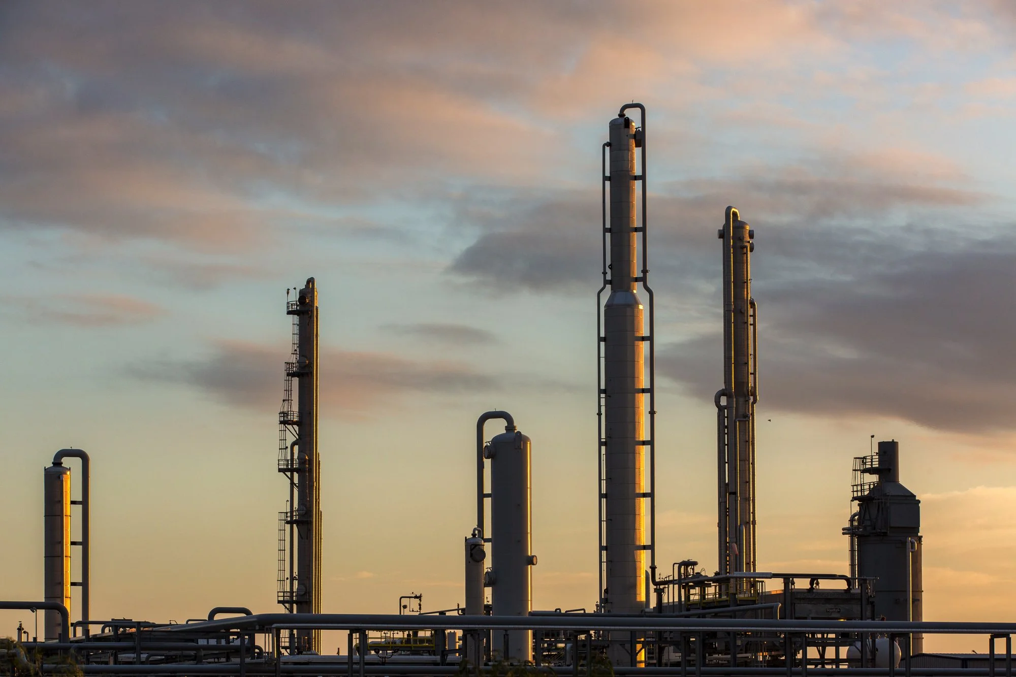 Industrial refinery with tall distillation columns under a cloudy sky at sunset.