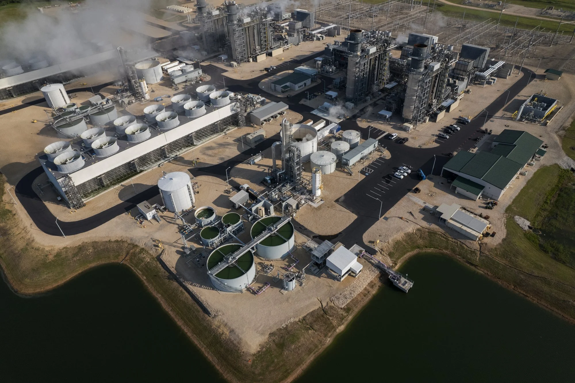 Aerial view of an industrial water treatment or waste management facility with large tanks, pipes, and processing units near a body of water.