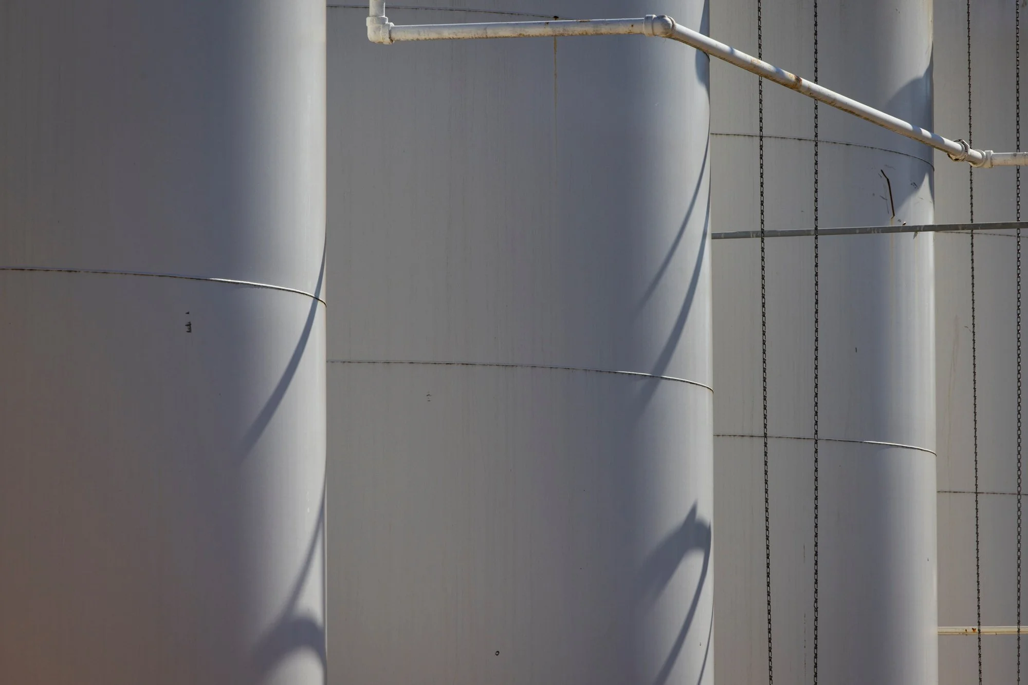 Close-up of large metallic storage tanks with pipes and chains attached.
