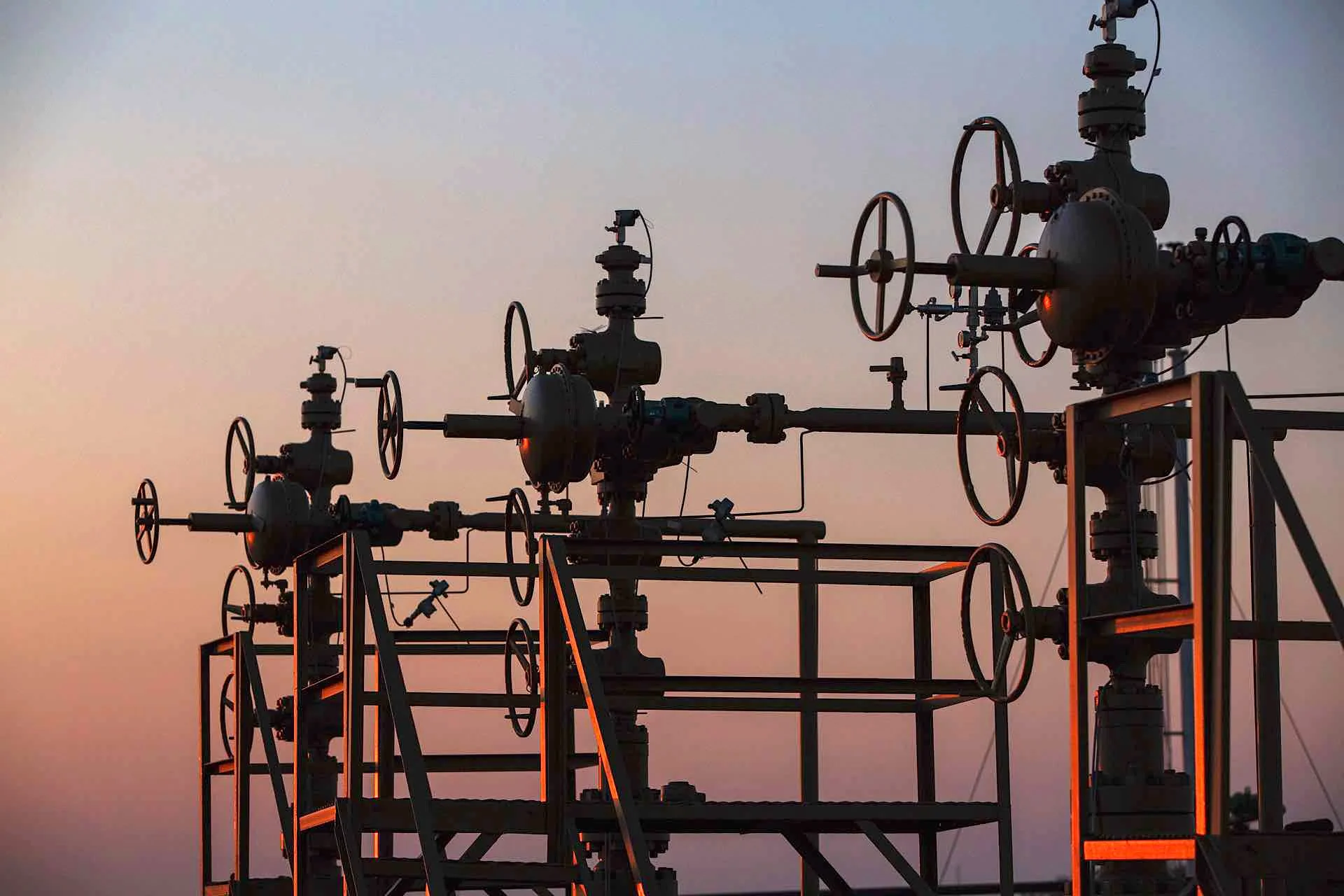 Industrial pipeline system with valves and gauges against a sunset sky.