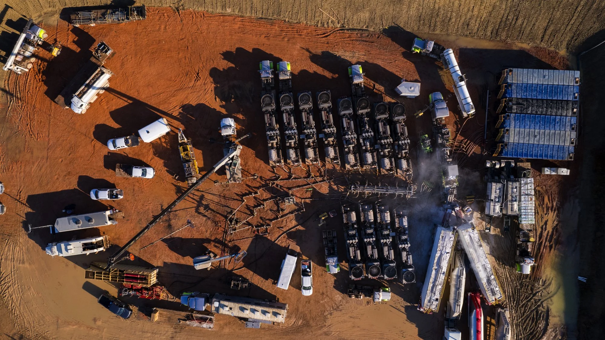 An aerial view of a construction site showing multiple trucks, construction vehicles, and equipment on a dirt surface.
