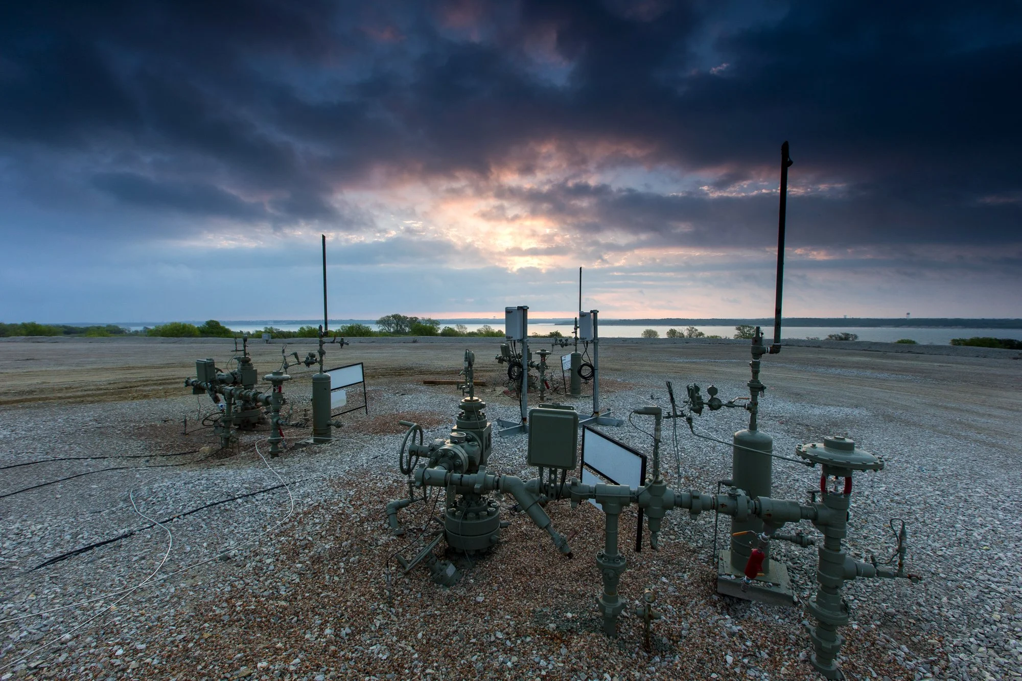 Deserted industrial gas measurement equipment under a cloudy sky at sunset with water in the background.