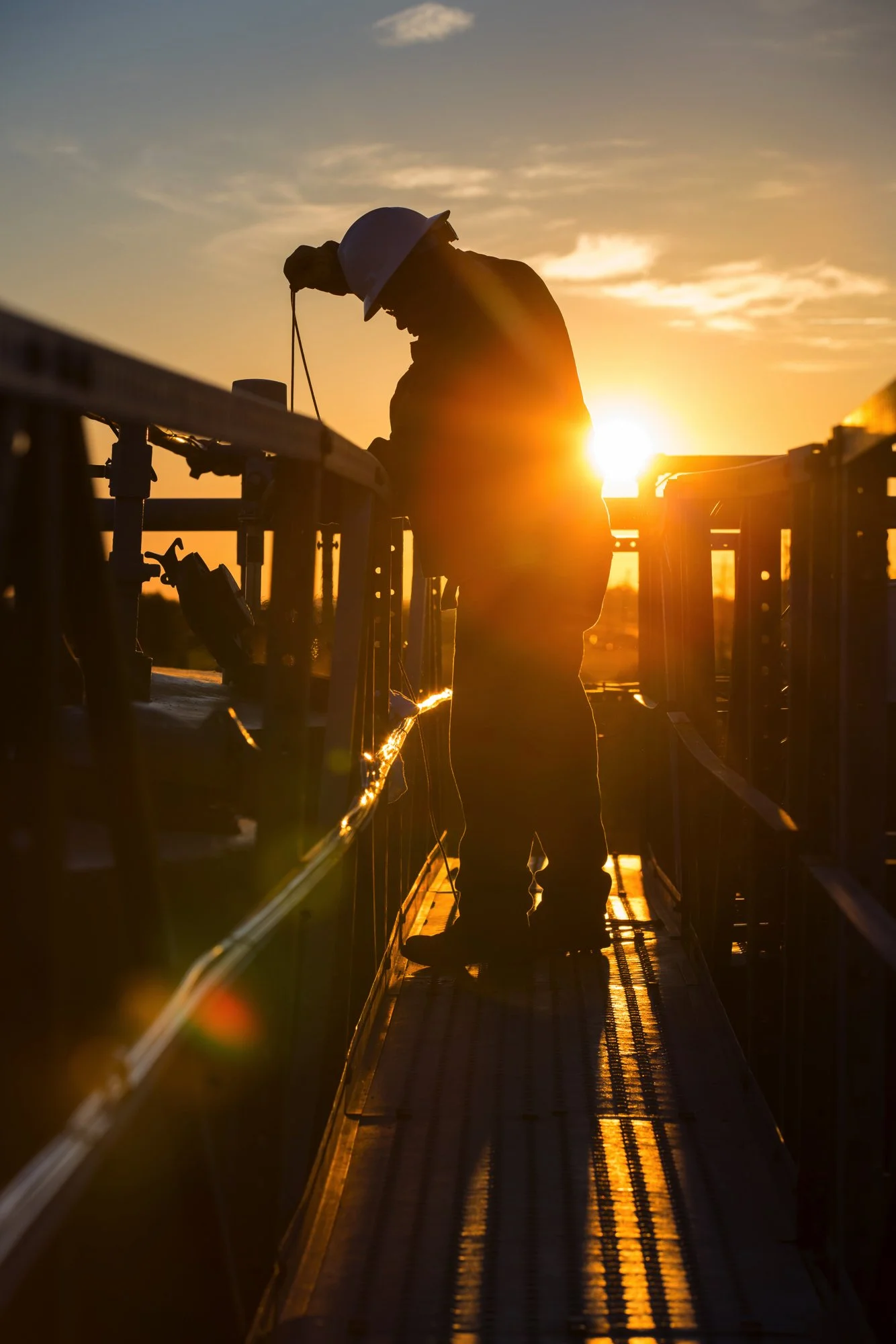 Silhouette of a worker wearing a safety helmet operating machinery at sunset.