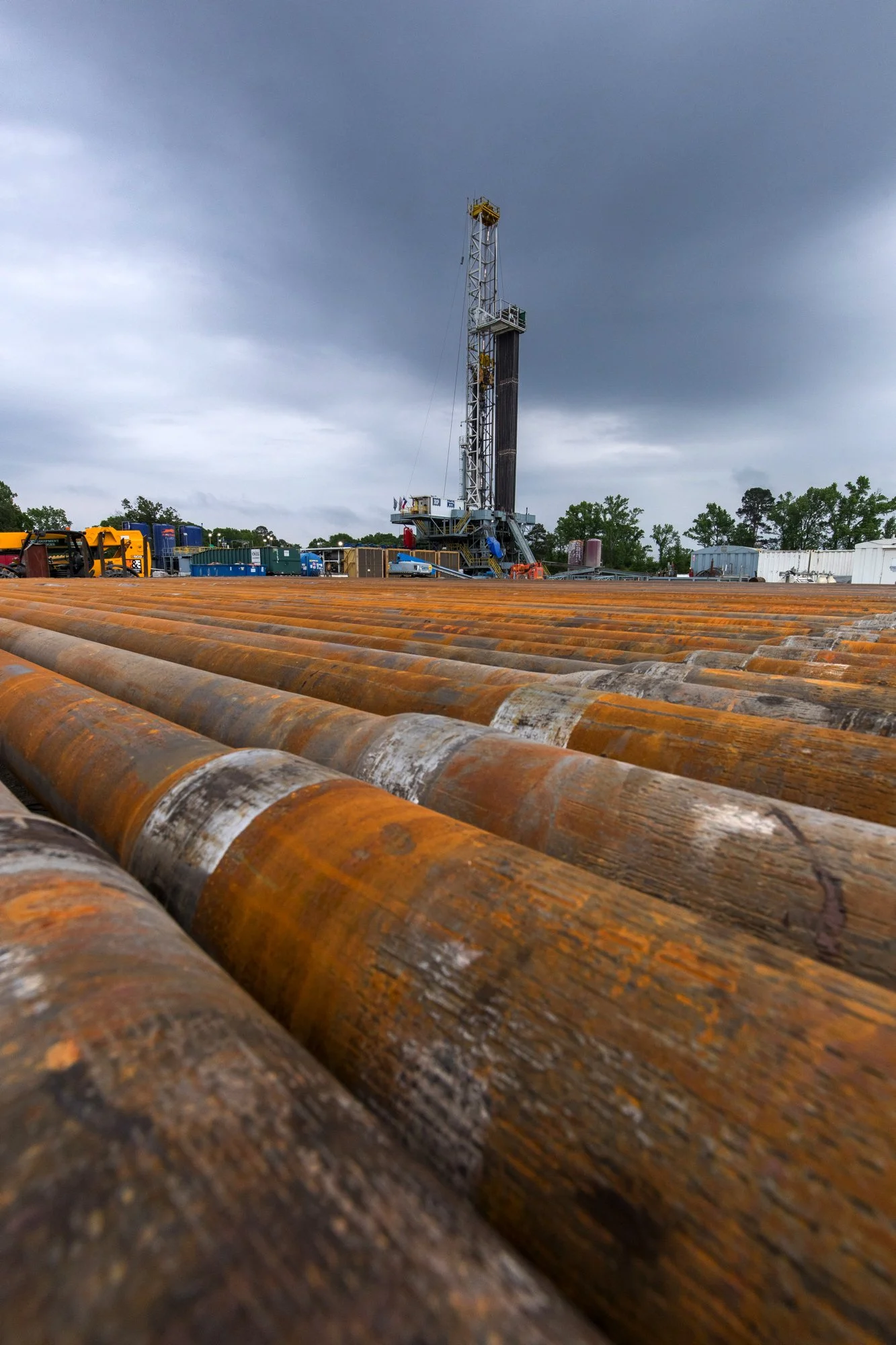 Oil rig drilling platform with rusted pipes in the foreground and a cloudy sky in the background.