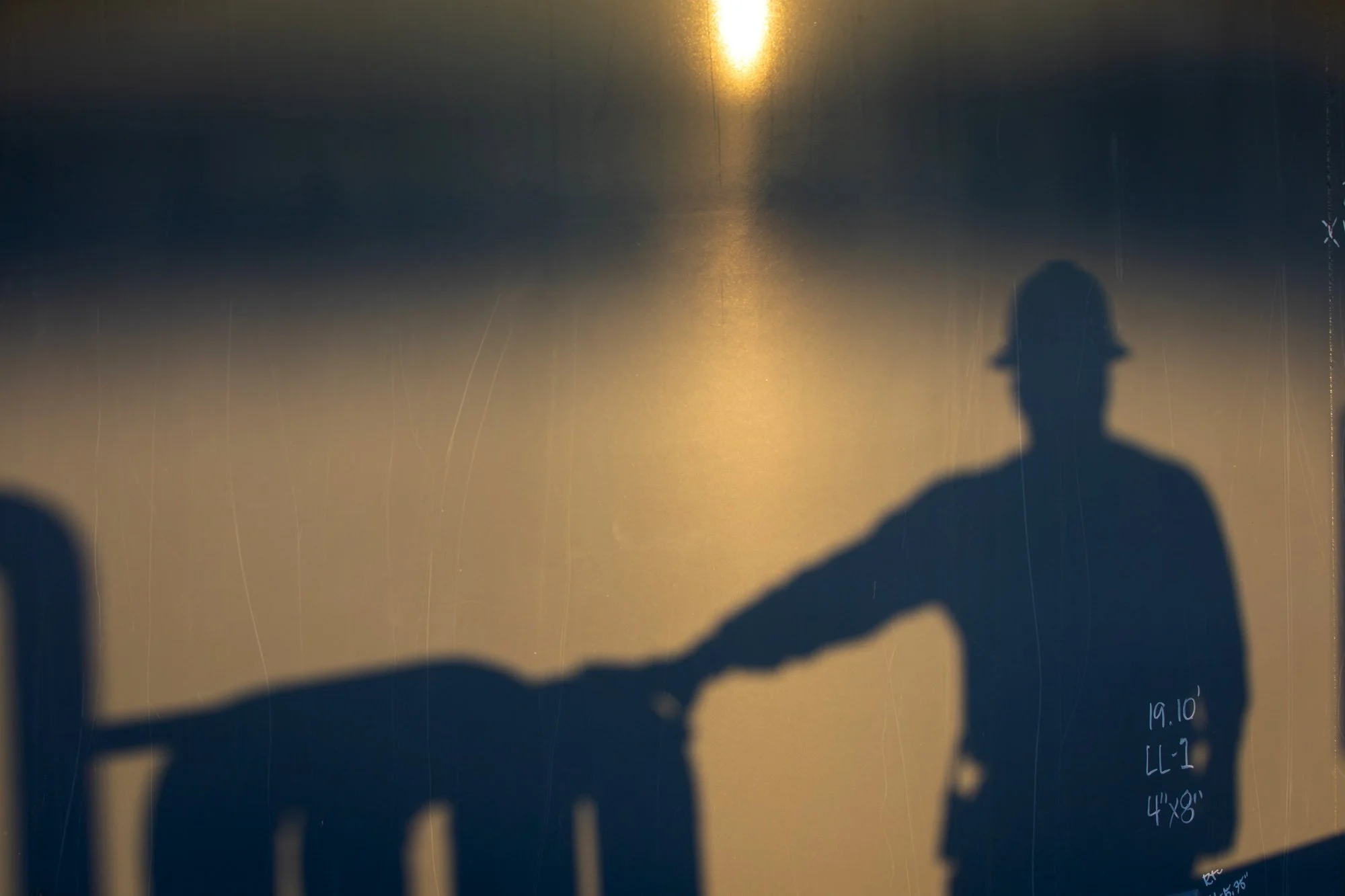 Silhouette of a person wearing a hard hat, holding another person's hand, with a bright light and reflection in the background.