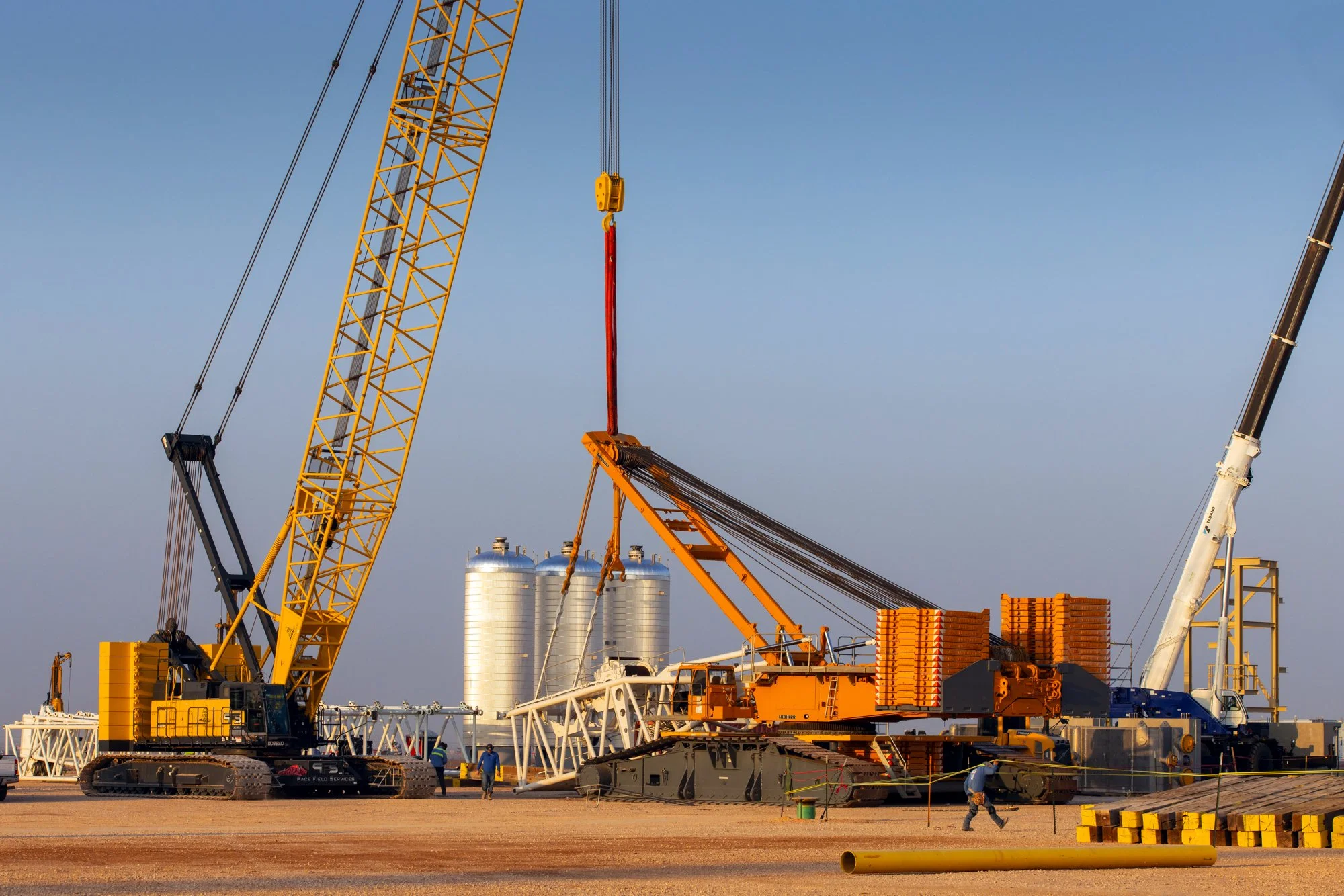 Large construction cranes working on a construction site during daytime with storage silos in the background.
