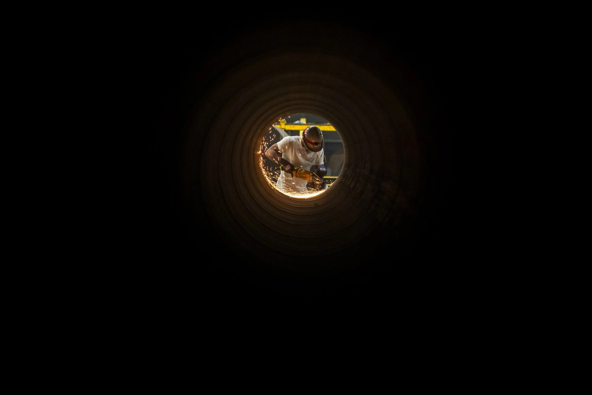 Worker welding inside a large pipe, sparks visible, safety helmet, protective gear.