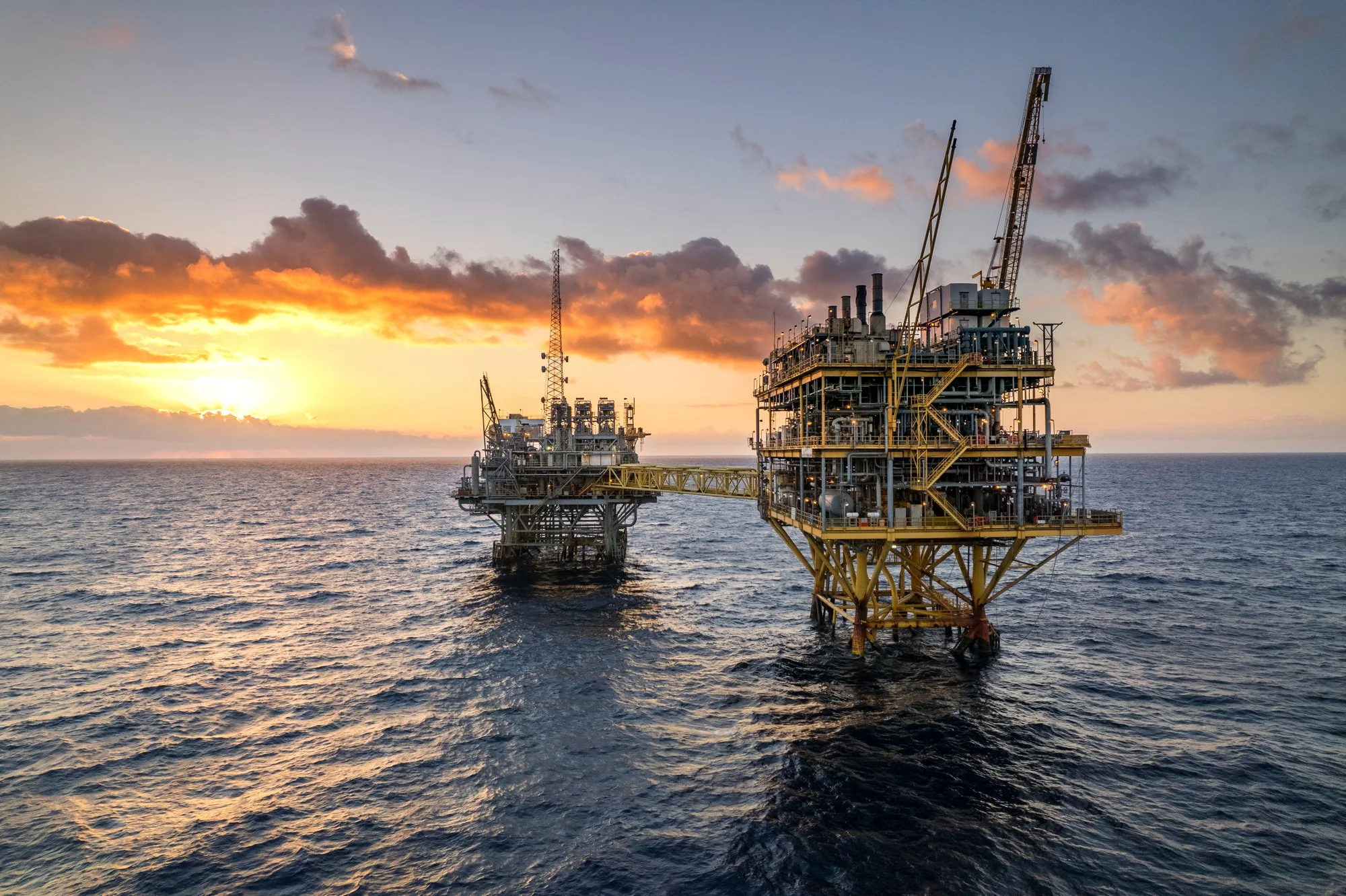 Offshore oil drilling platform in the ocean at sunset with a partly cloudy sky.