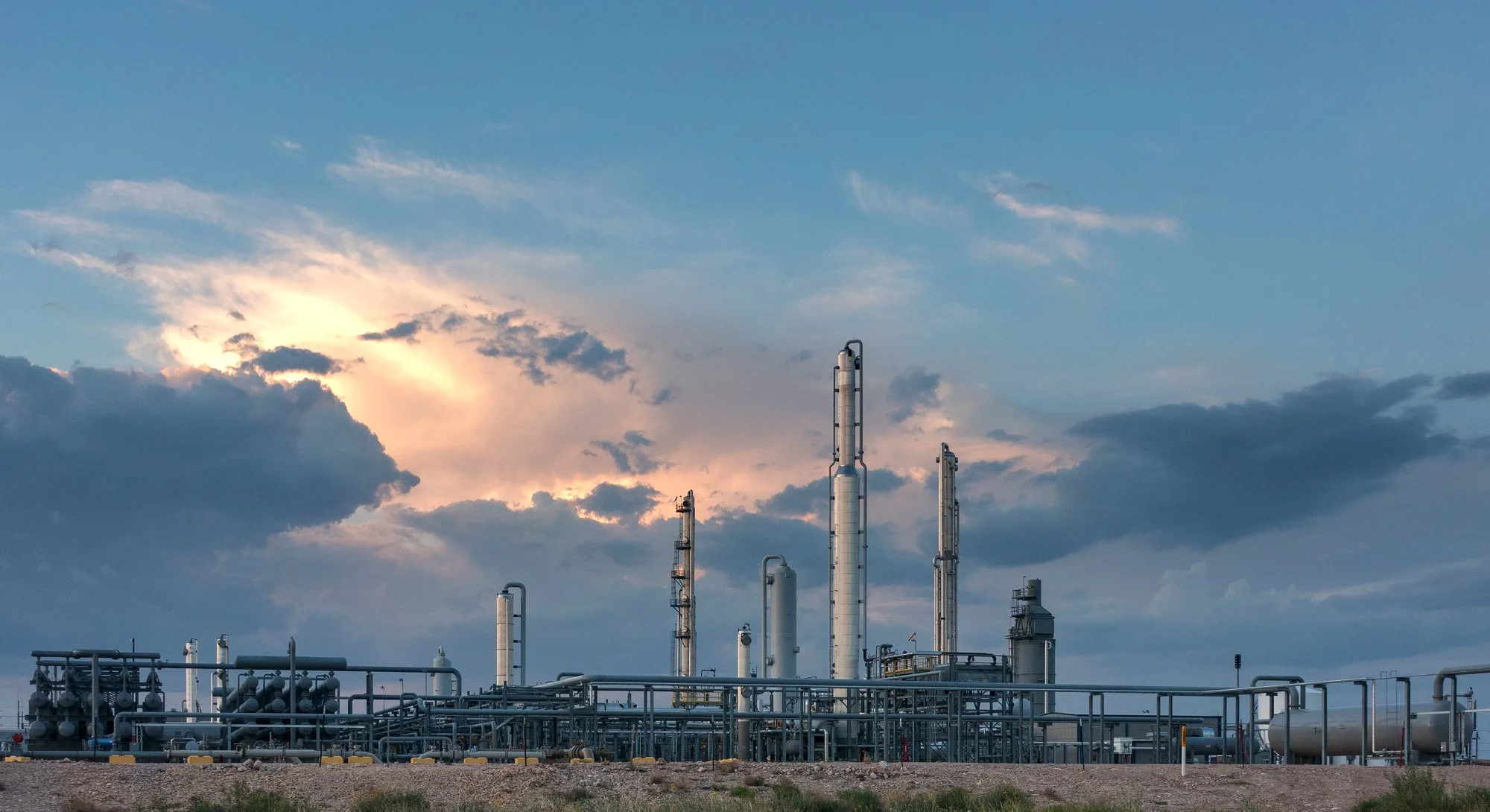 Large industrial oil refinery with pipes and tall towers under a partly cloudy sky.