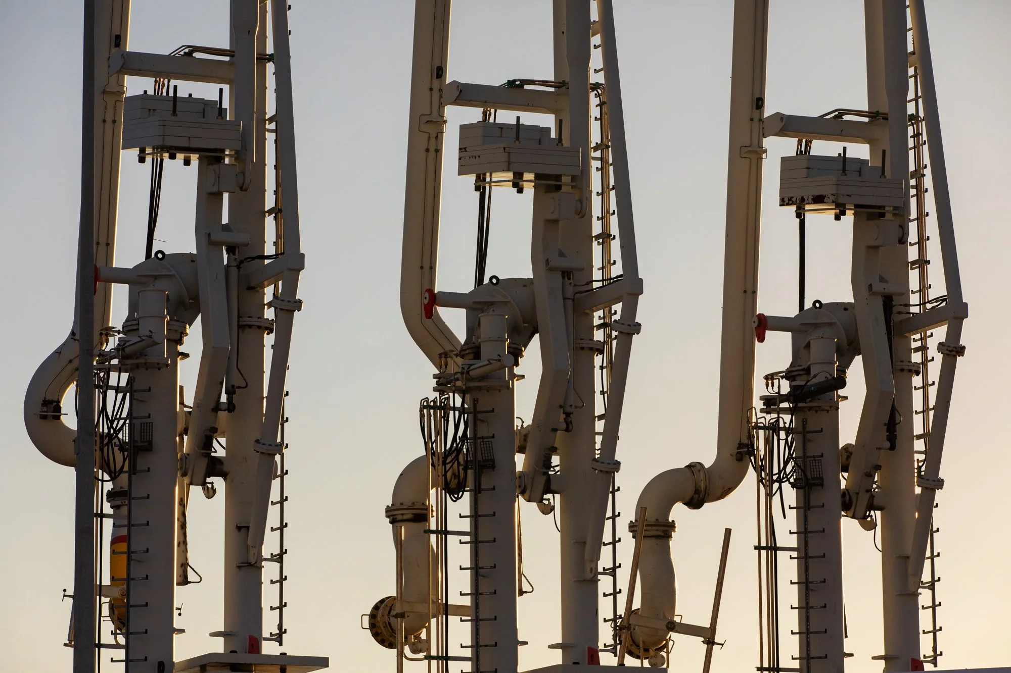 Multiple industrial pipelines and machinery against a neutral sky background.