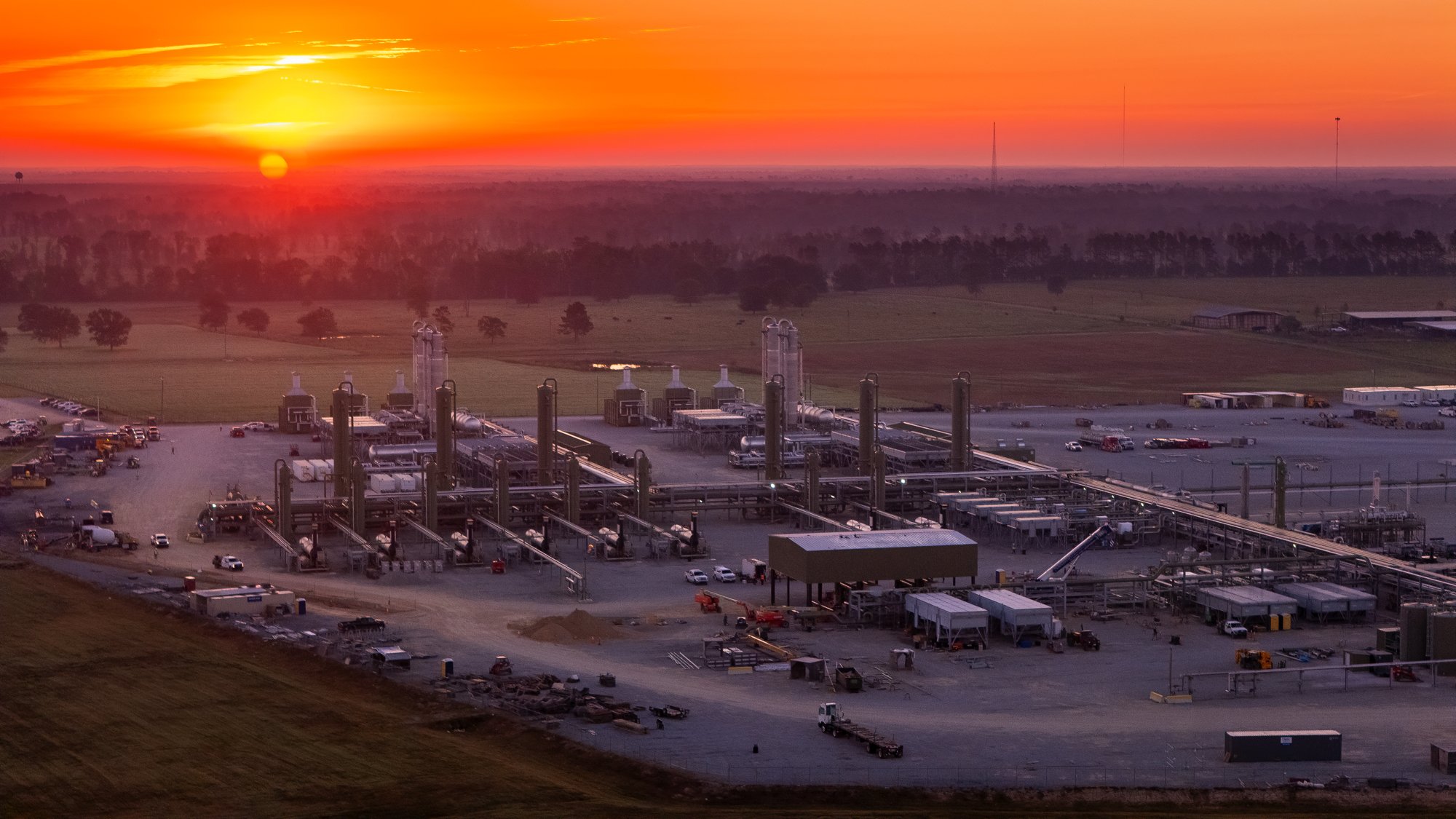 Oil refinery with tanks, pipes, and smoke stacks during sunset.