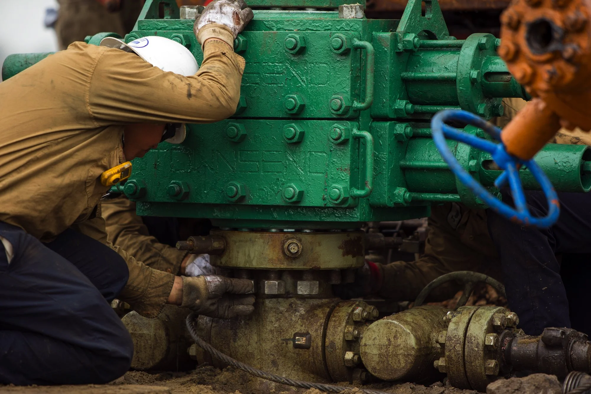Workers in safety gear inspecting a large green industrial valve or pump at a construction or maintenance site.