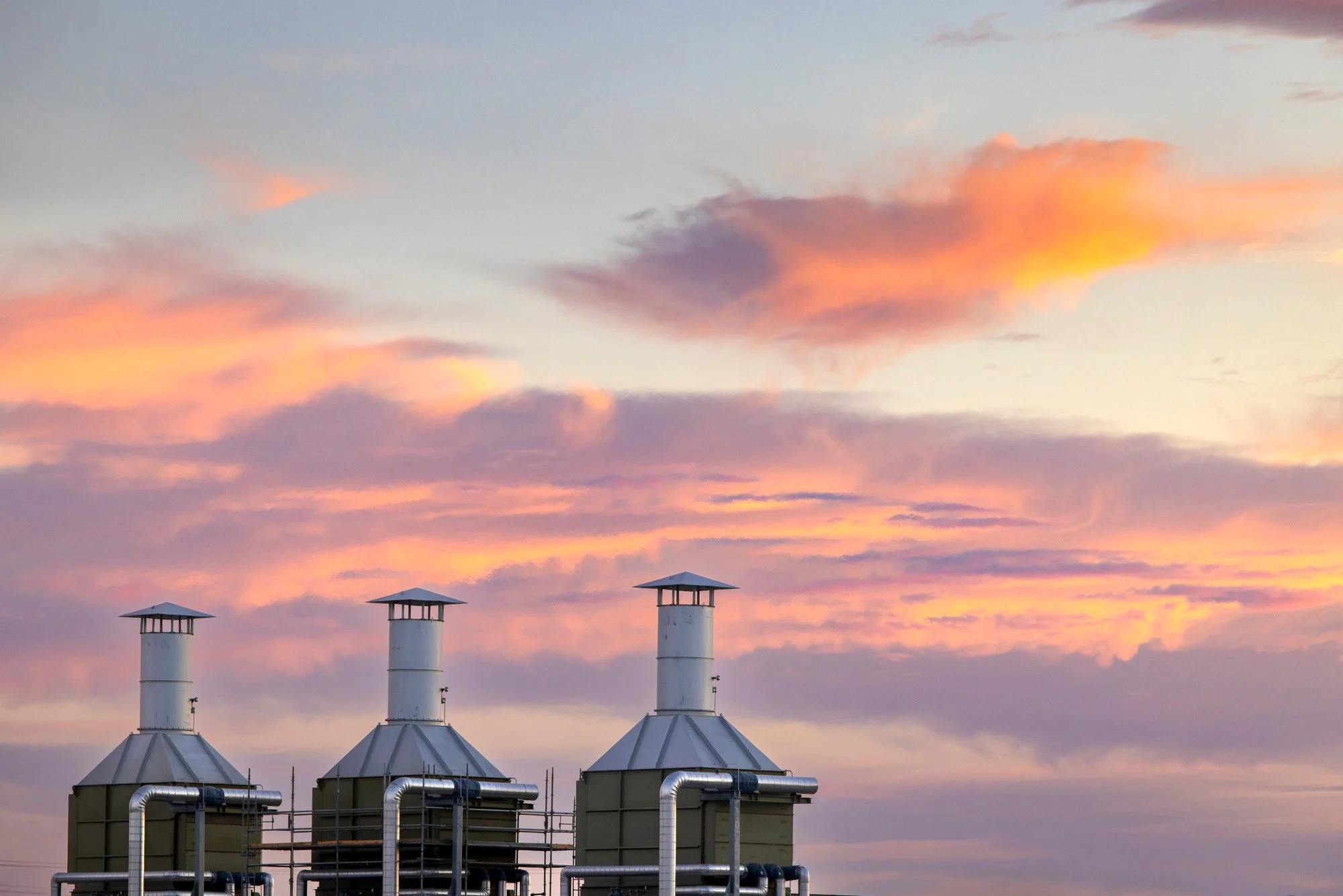 Industrial cooling towers with pipes under a colorful sky at sunset.