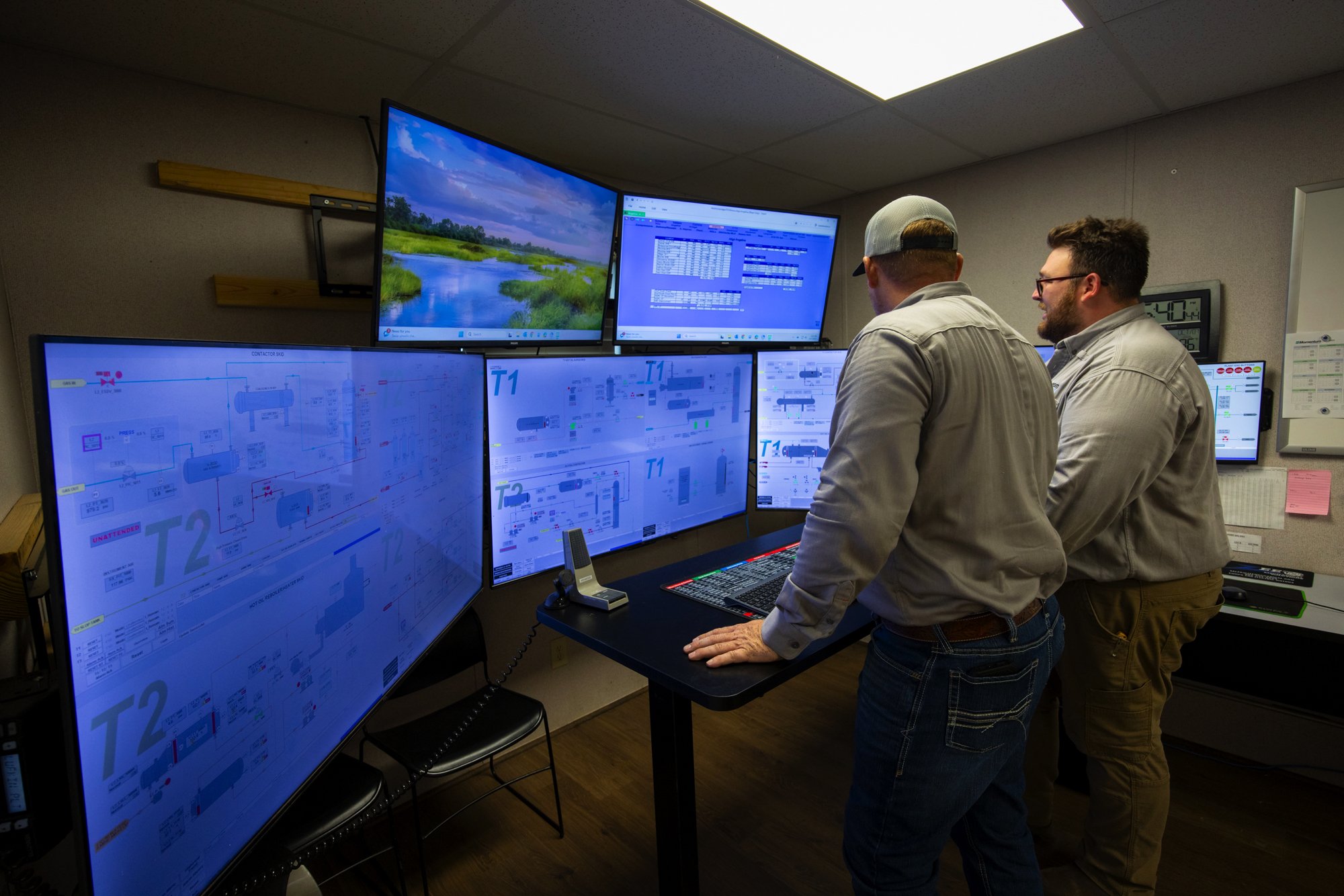 Two men working in a control room with multiple monitors displaying technical diagrams and data.