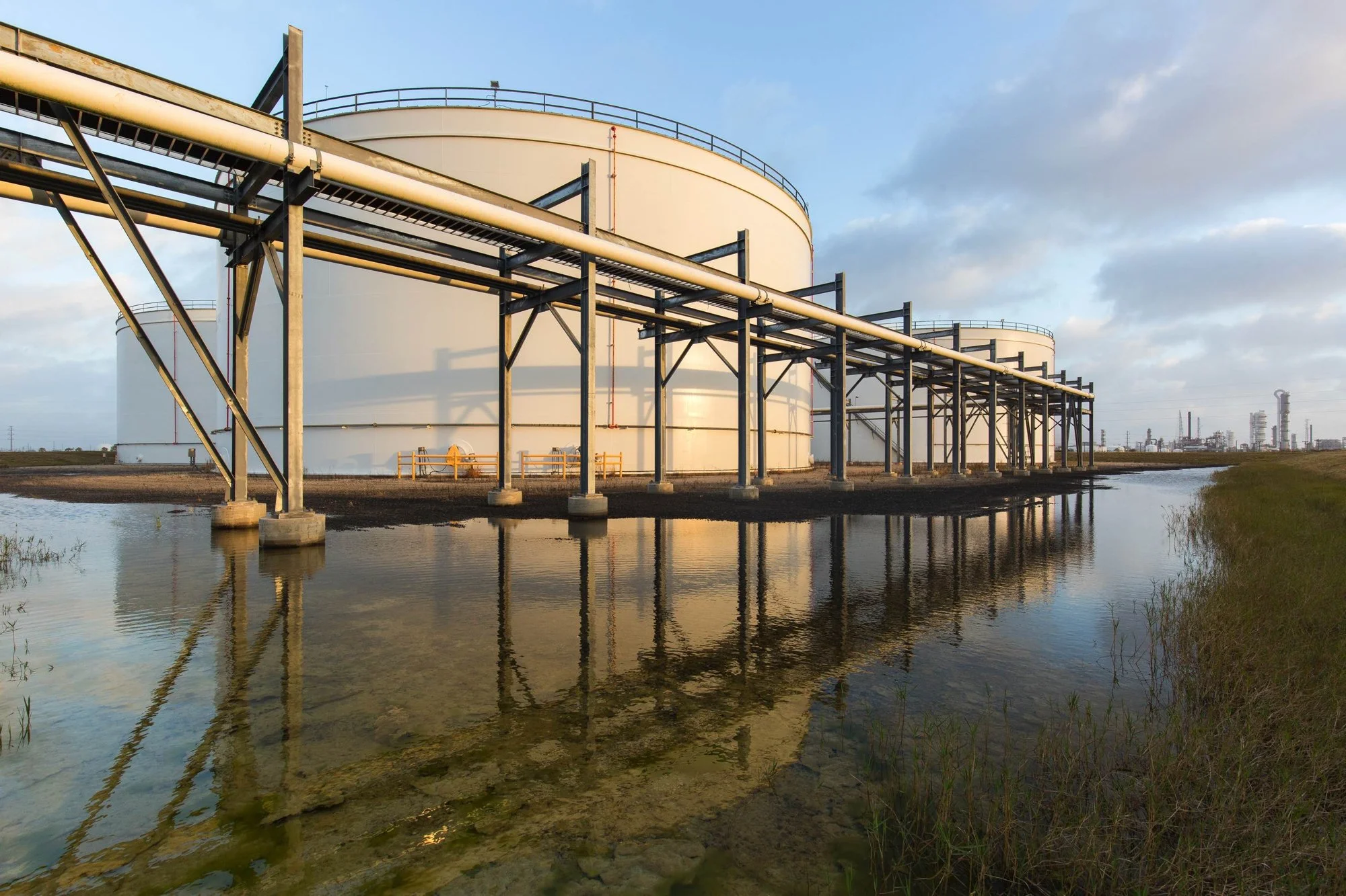 Oil storage tanks with a pipeline and reflection in water, in an industrial area