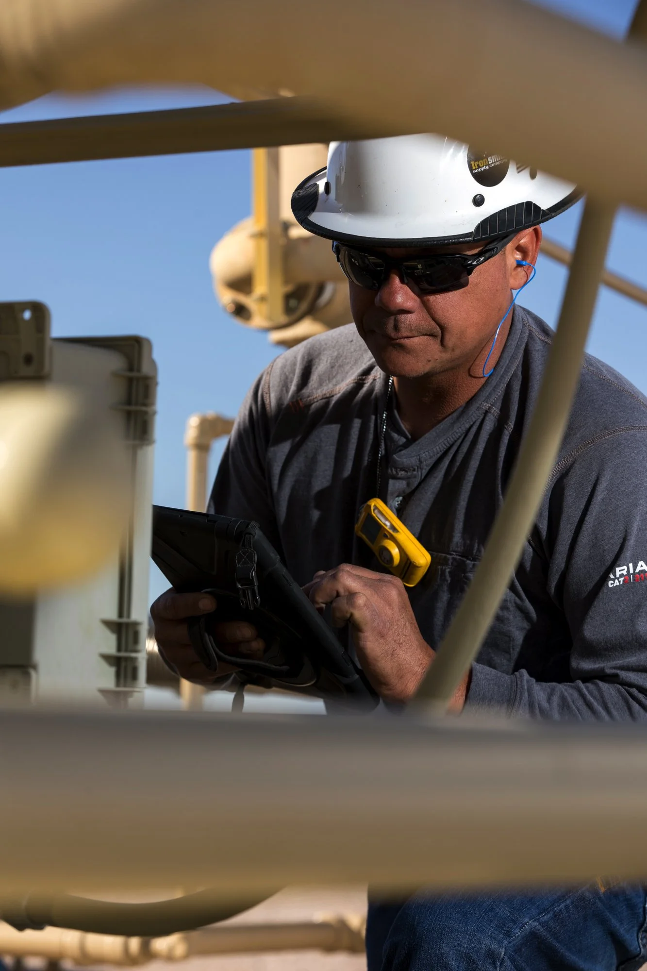 Utility worker wearing a helmet and sunglasses uses a tablet or device outdoors.