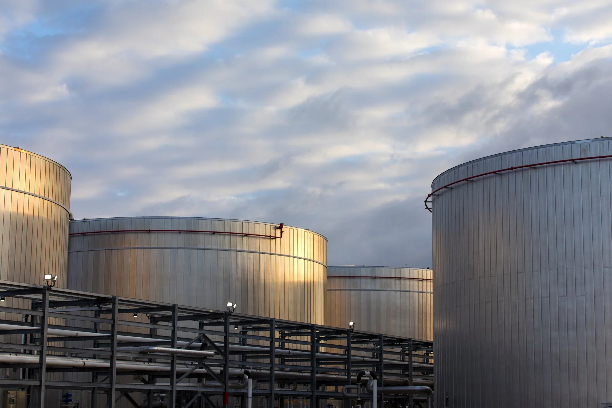 Industrial storage tanks with pipes and metal framework under a partly cloudy sky.
