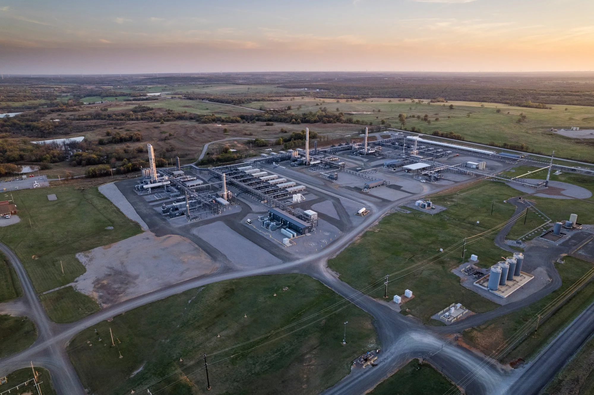 Aerial view of a large industrial facility, possibly a power plant or manufacturing complex, surrounded by open fields and rural landscape at sunset.