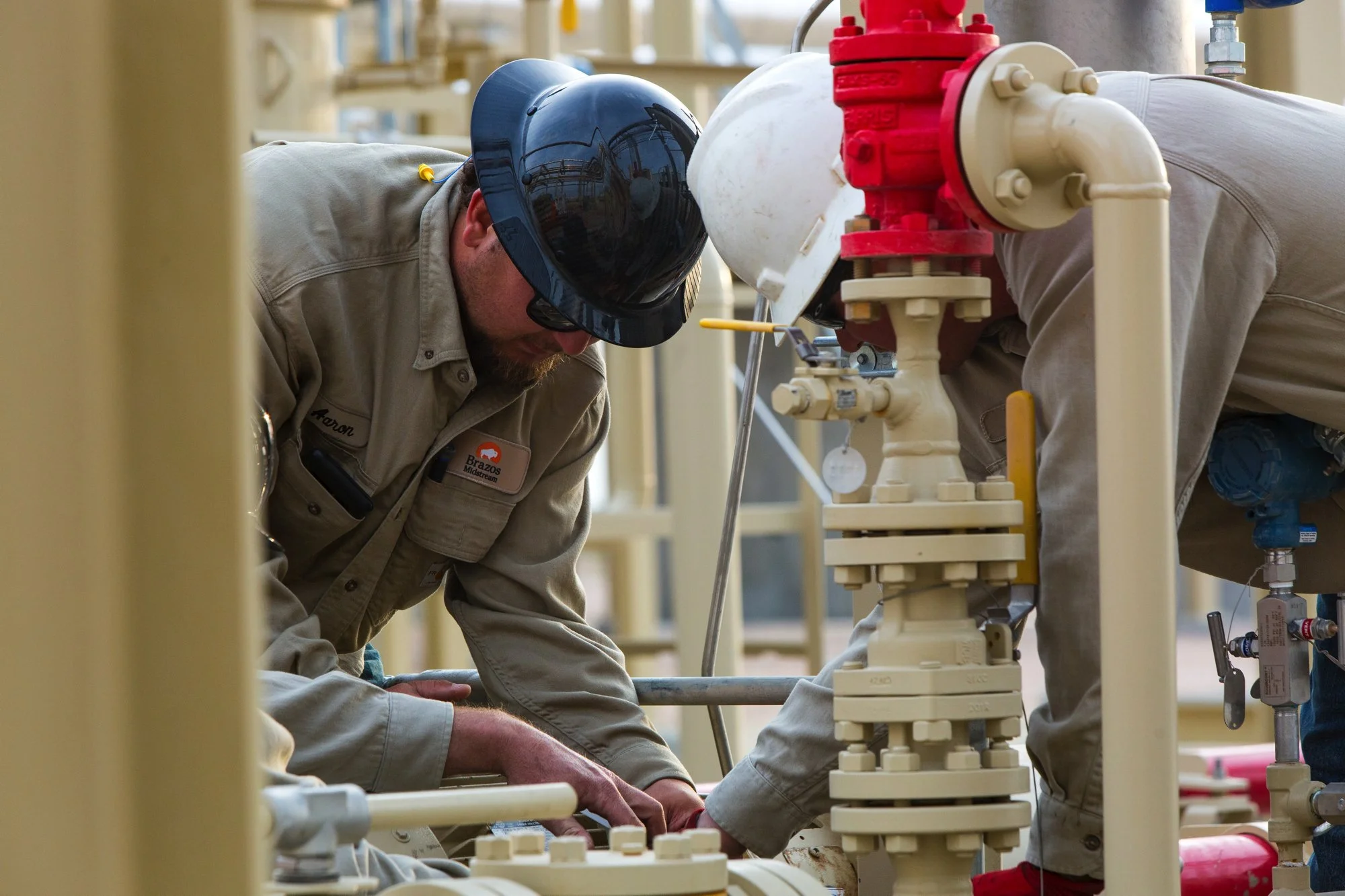 Two workers wearing uniforms and safety helmets working on industrial pipes.