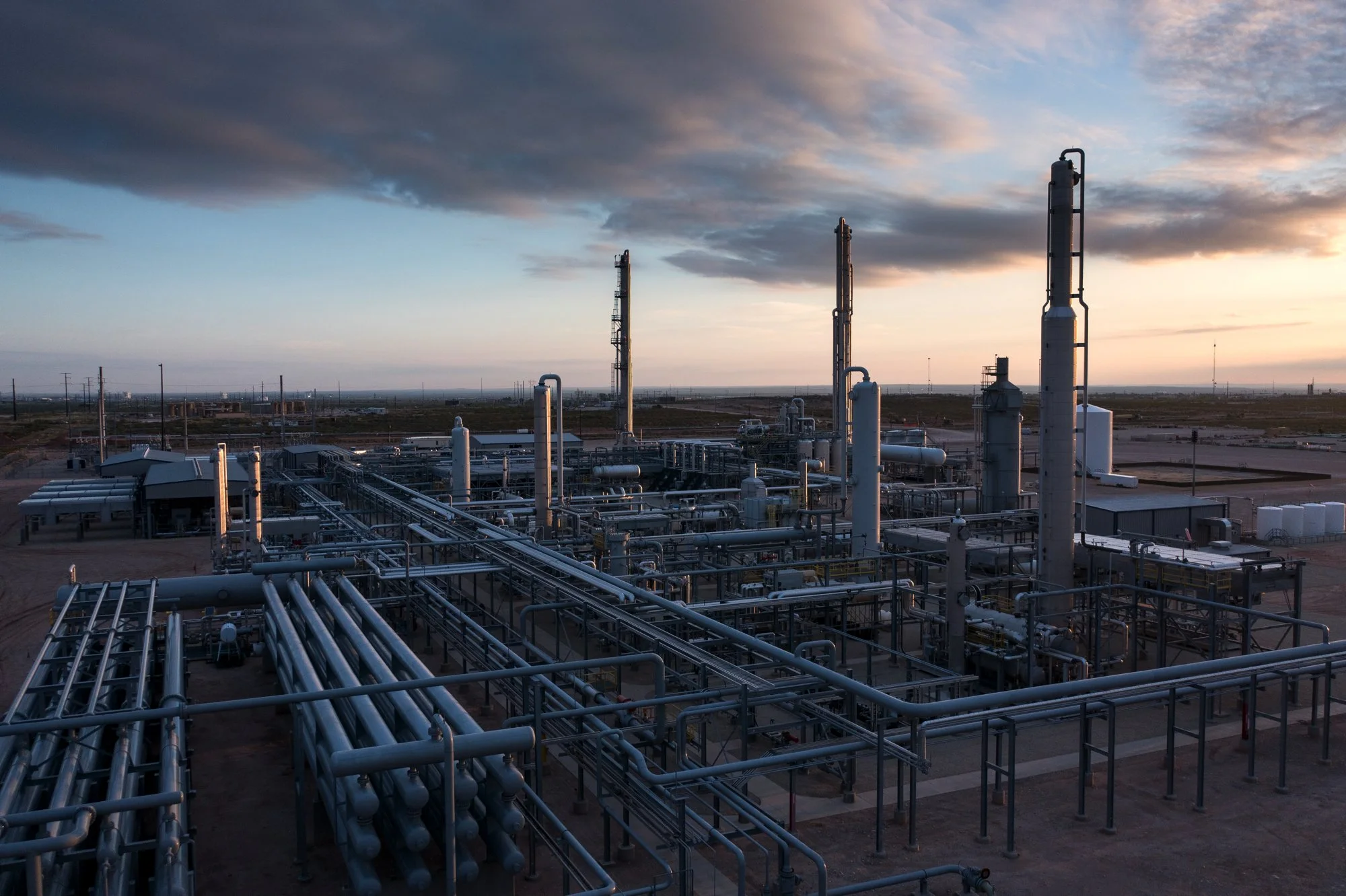 An industrial oil refinery with pipelines and distillation towers at sunset.