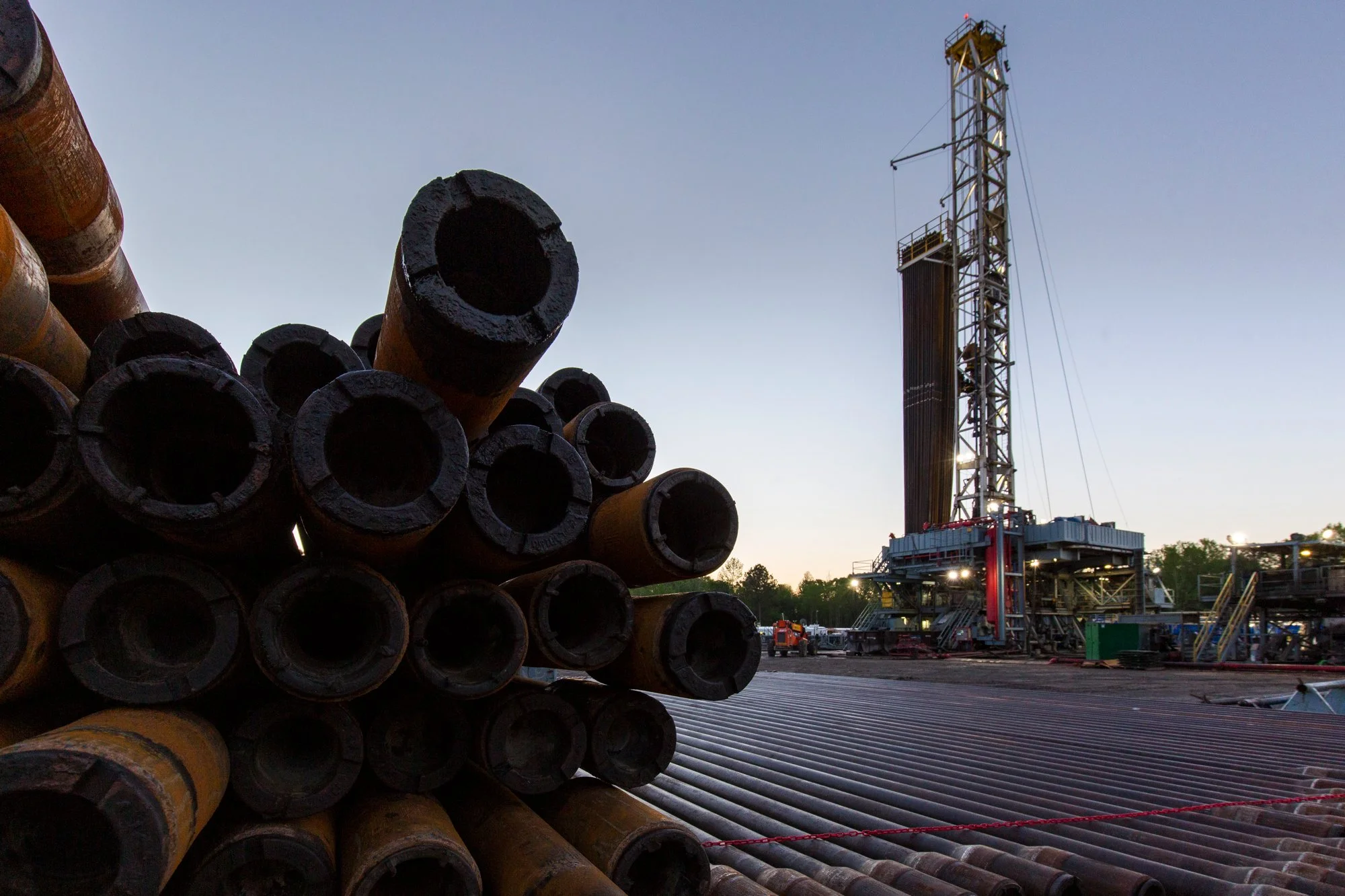 Oil drilling rig with stacked drill pipes in the foreground at sunset.